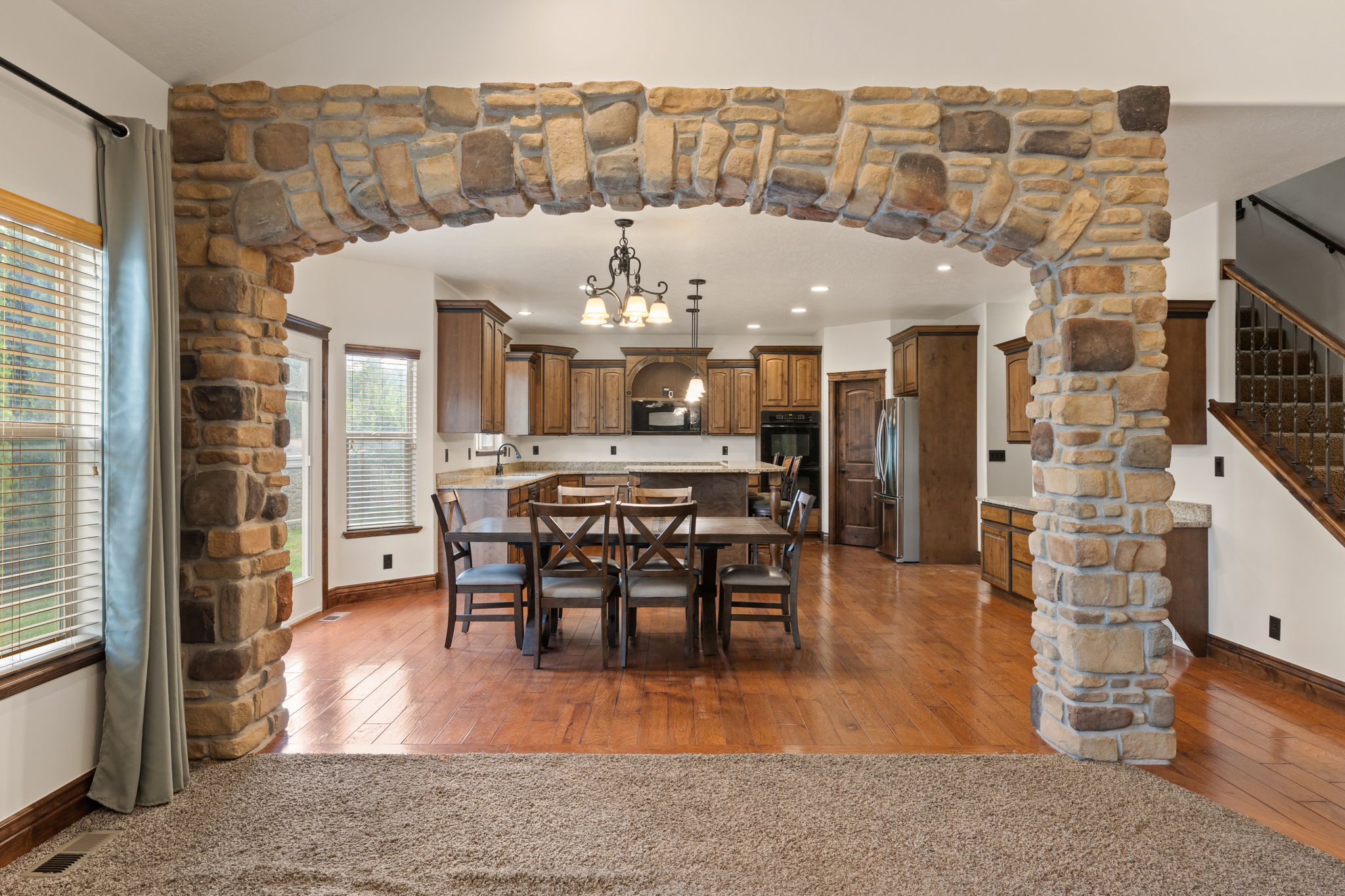 Stone archway framing an expansive kitchen and dining area with wood-finish flooring