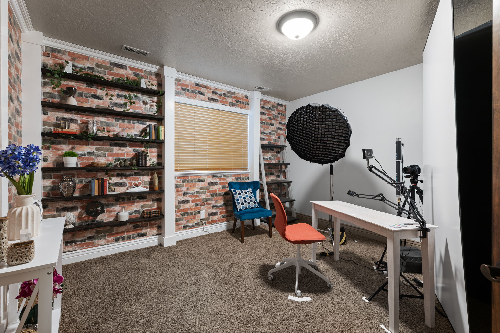 Room featuring a decorative brick-patterned accent wall with built-in shelving, a single window with blinds, and carpeted flooring