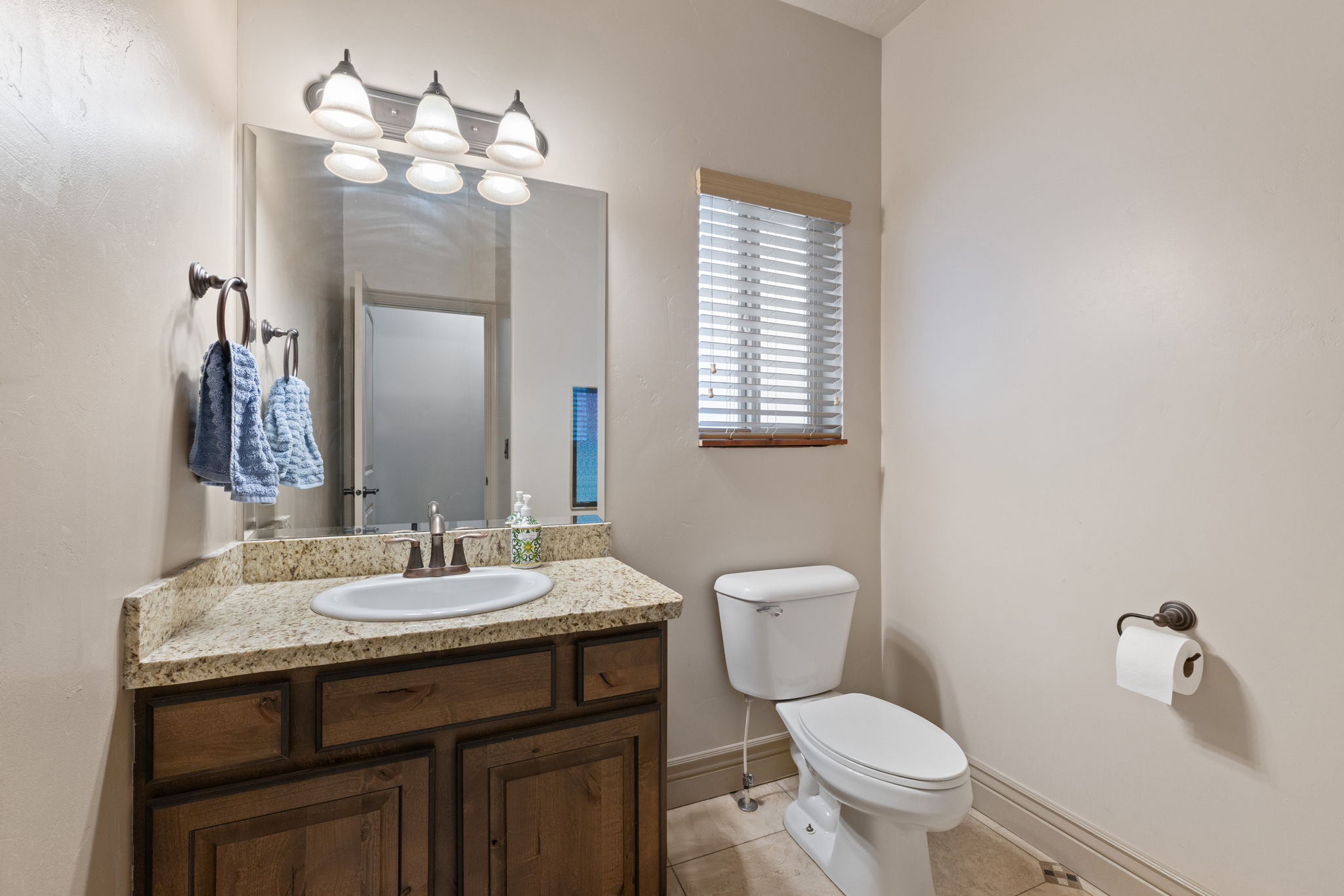 Bathroom featuring a wood-finish vanity with an oval undermount sink, a light-toned countertop, and a wall-mounted mirror