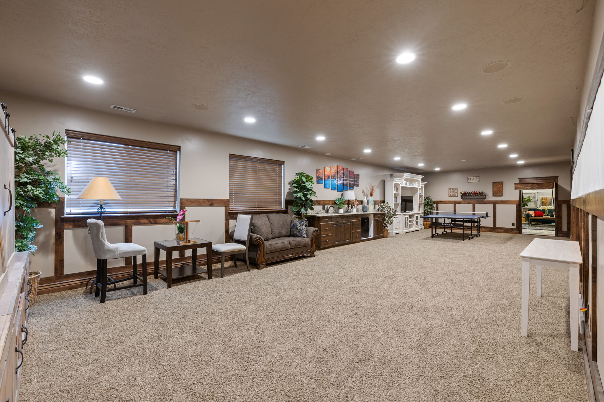 Spacious interior room featuring extensive carpet flooring, recessed ceiling lighting, and multiple windows with horizontal blinds