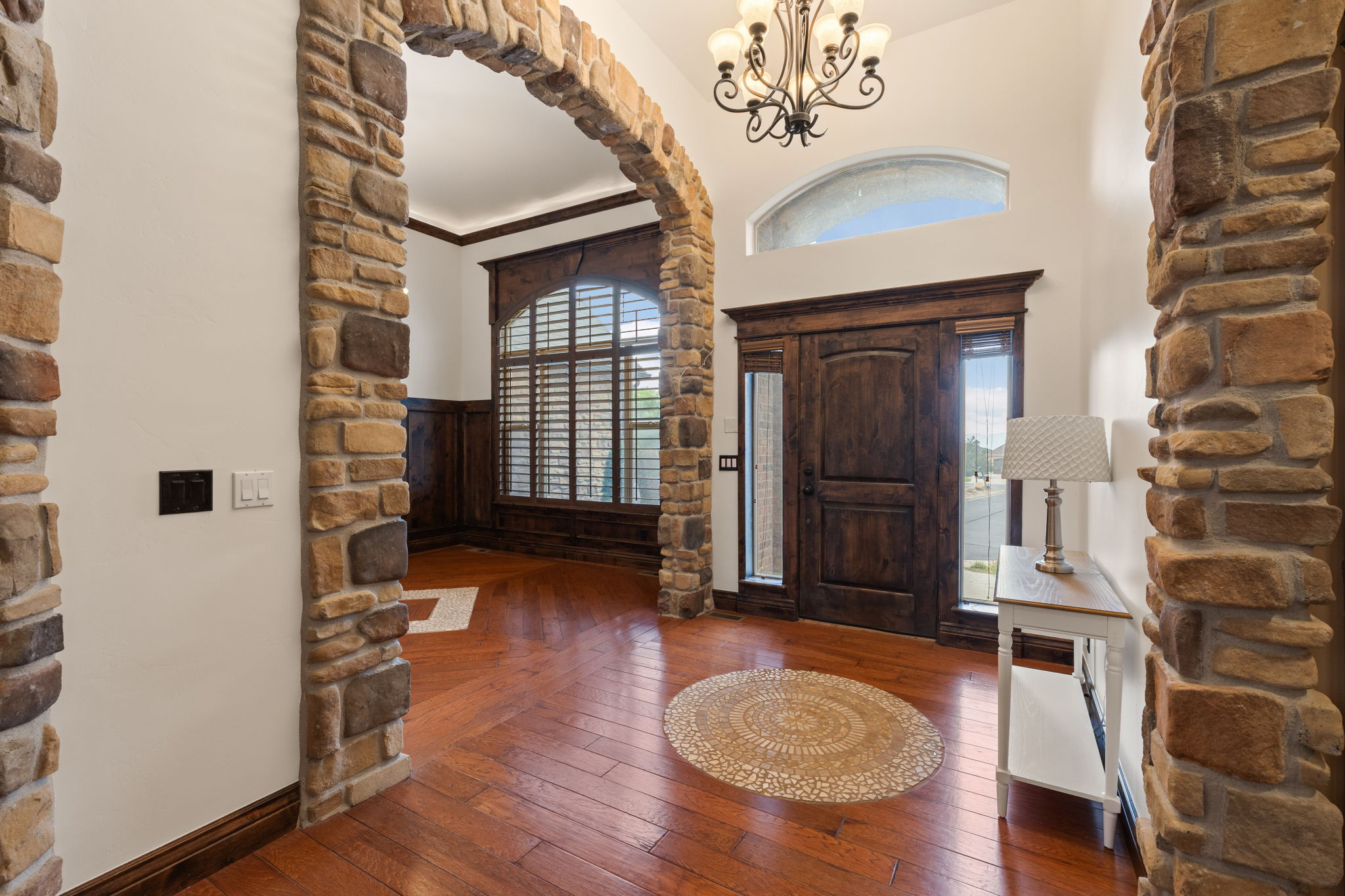 Foyer featuring a double door entry with sidelights, an arched transom window, wood-finish flooring, a stone archway, and a wrought iron chandelier