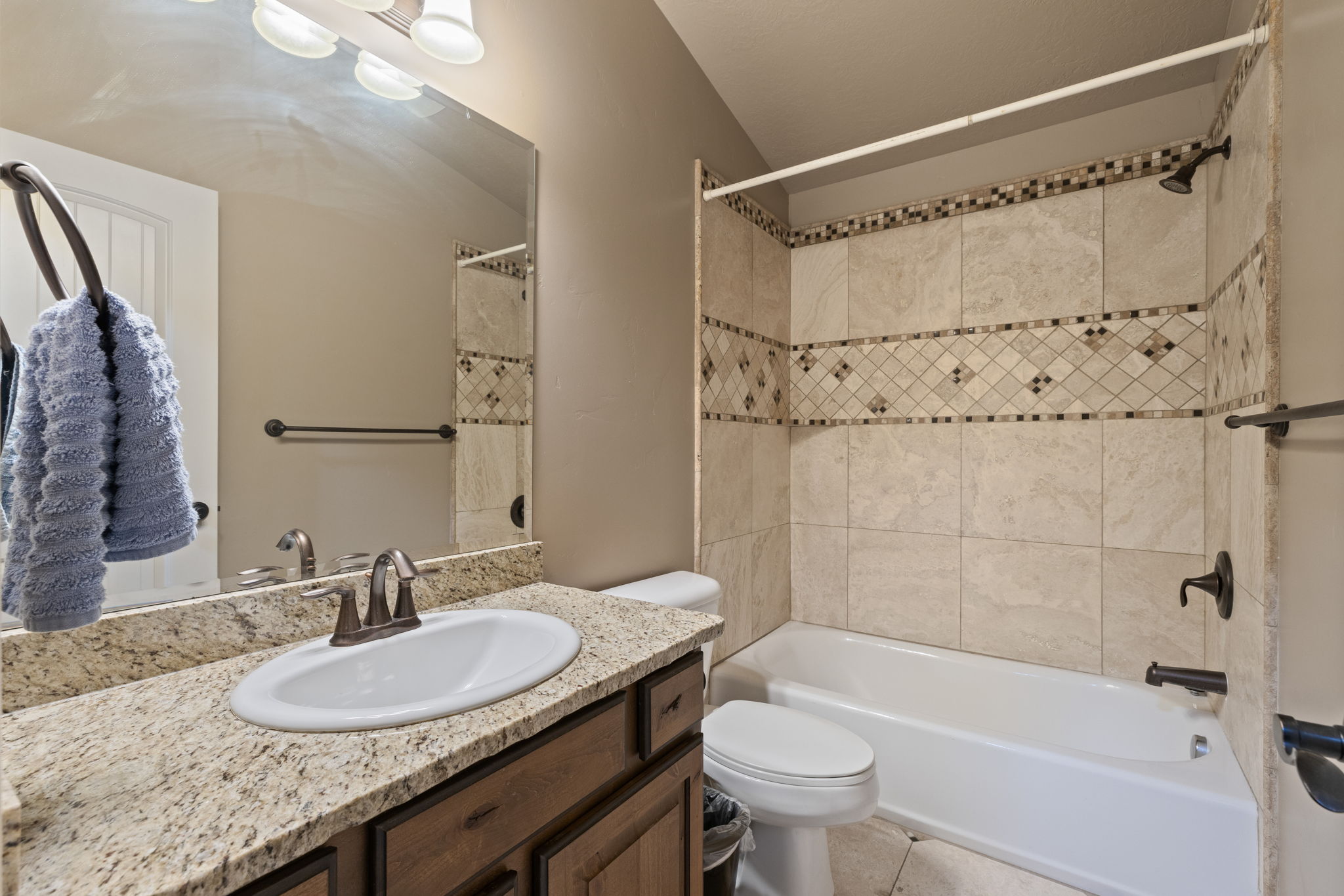 Bathroom featuring a tub/shower combination with tile surround and decorative accents, a single vanity with granite-look countertop, integrated sink, and an overhead light fixture
