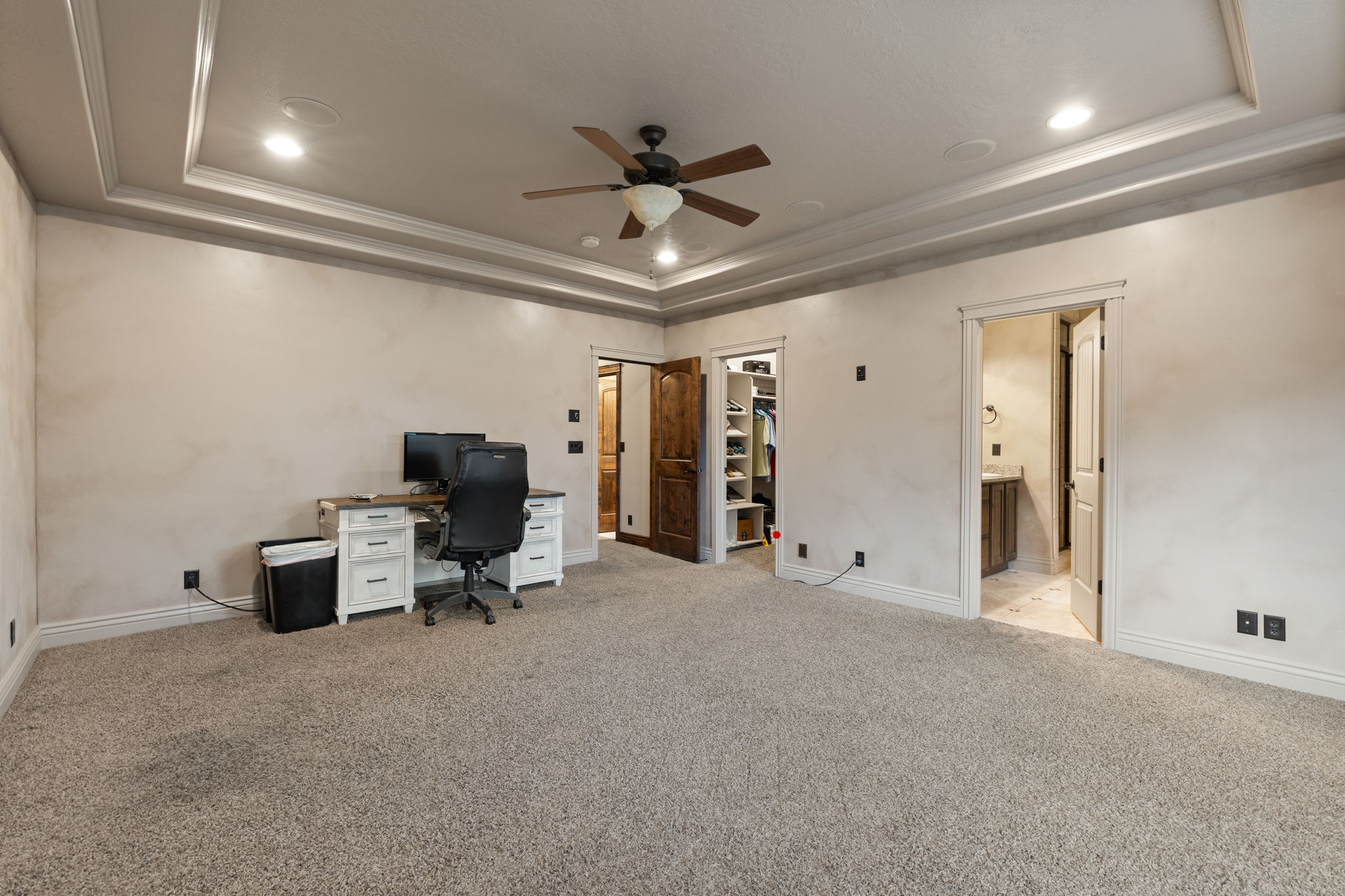 Spacious carpeted room featuring a detailed tray ceiling, recessed lighting, and a dark wood-finish ceiling fan