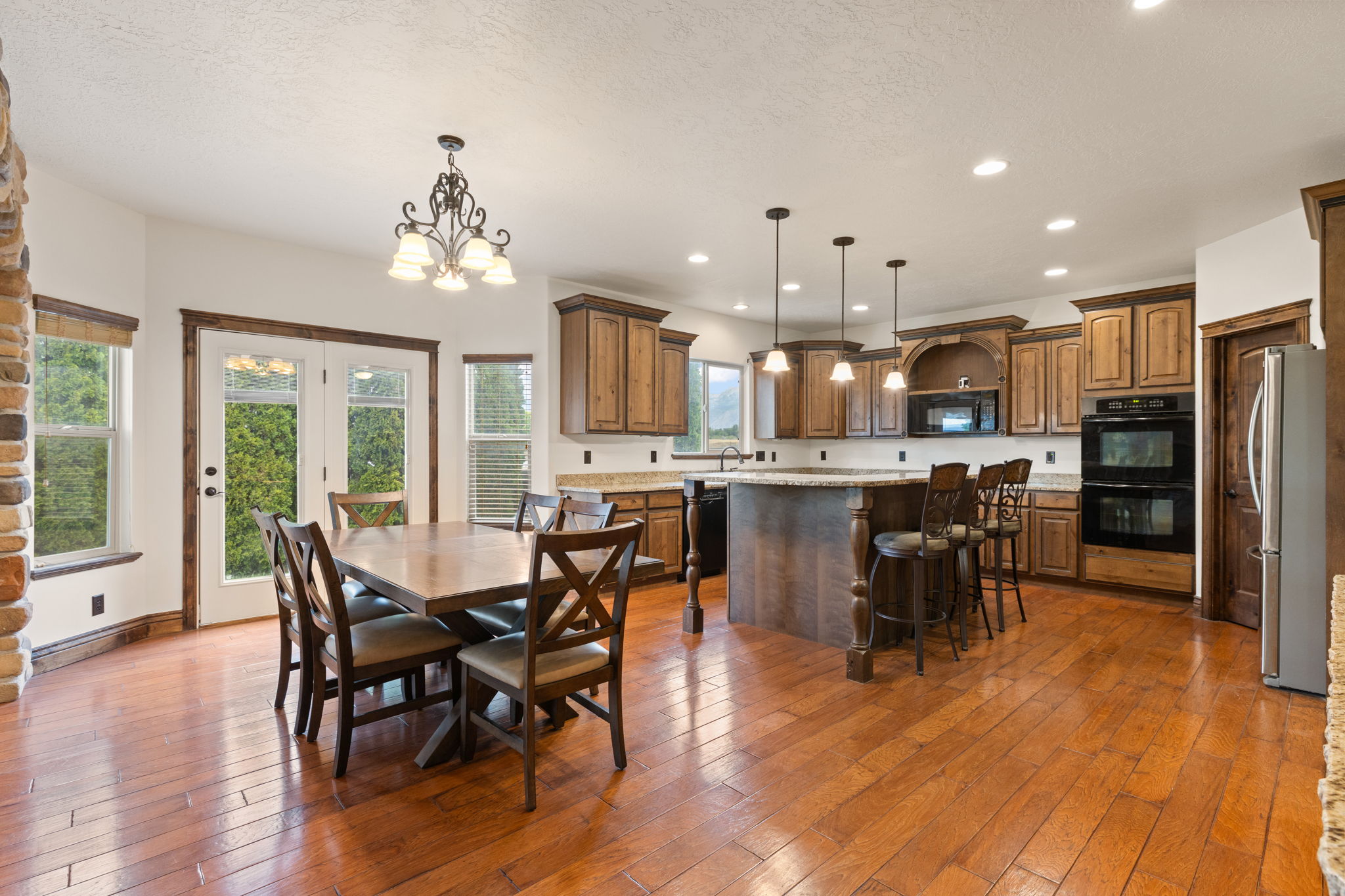 Spacious kitchen and dining area featuring wood-finish flooring, a built-in double oven, a central island with bar seating, and warm wood cabinetry
