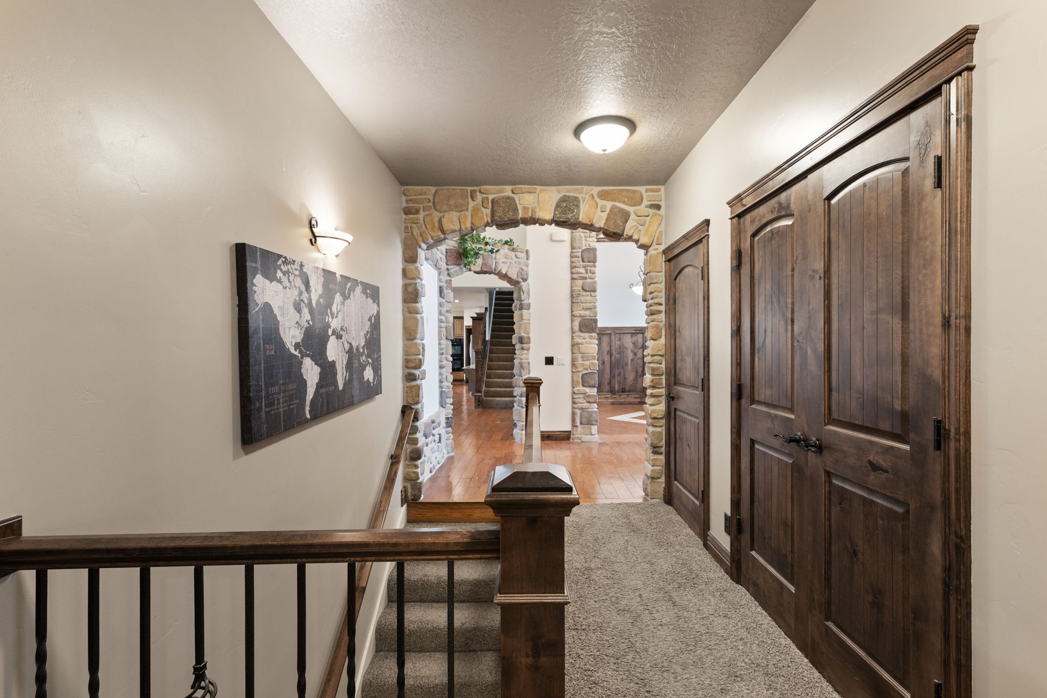 Hallway featuring textured carpeting, stone archway, and wood-paneled doors with dark hardware