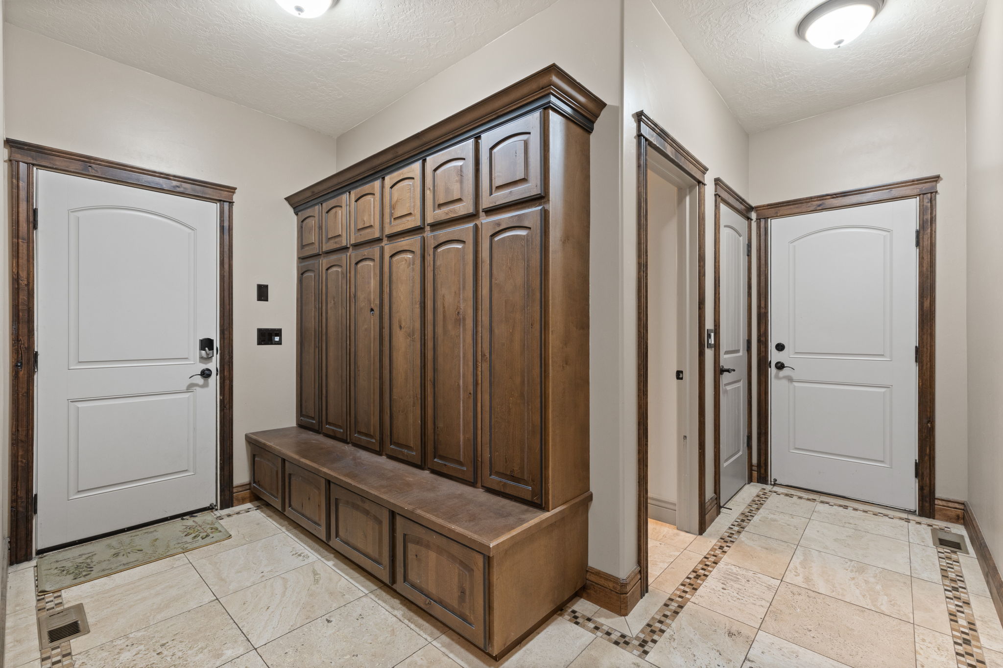 Entryway featuring built-in wood cabinetry with storage bench, white panel doors with dark hardware, natural stone tile flooring, and decorative tile accents