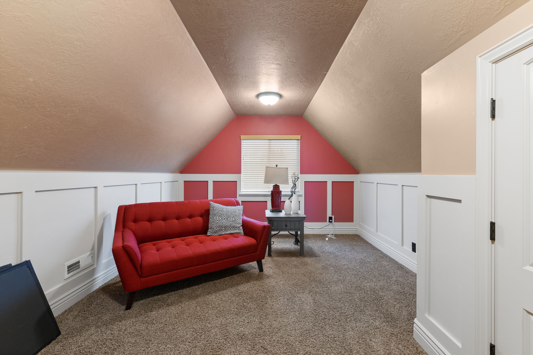 Carpeted room featuring a white paneled wainscoting, sloped ceilings, a window with blinds, and a built-in overhead light fixture
