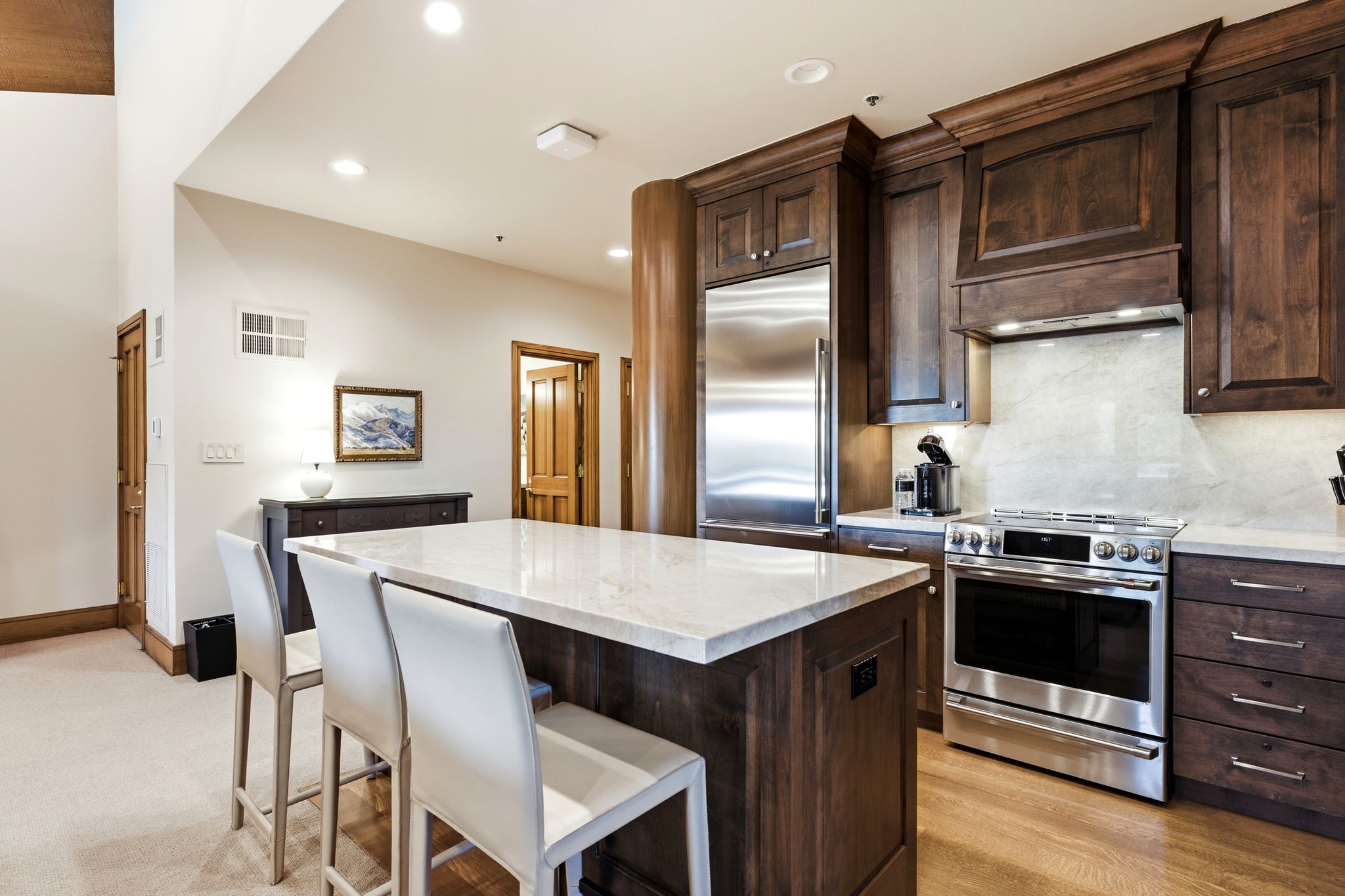 Kitchen featuring a central island with a light-toned countertop, stainless steel appliances, dark wood cabinetry, light wood-finish flooring, and recessed ceiling lighting
