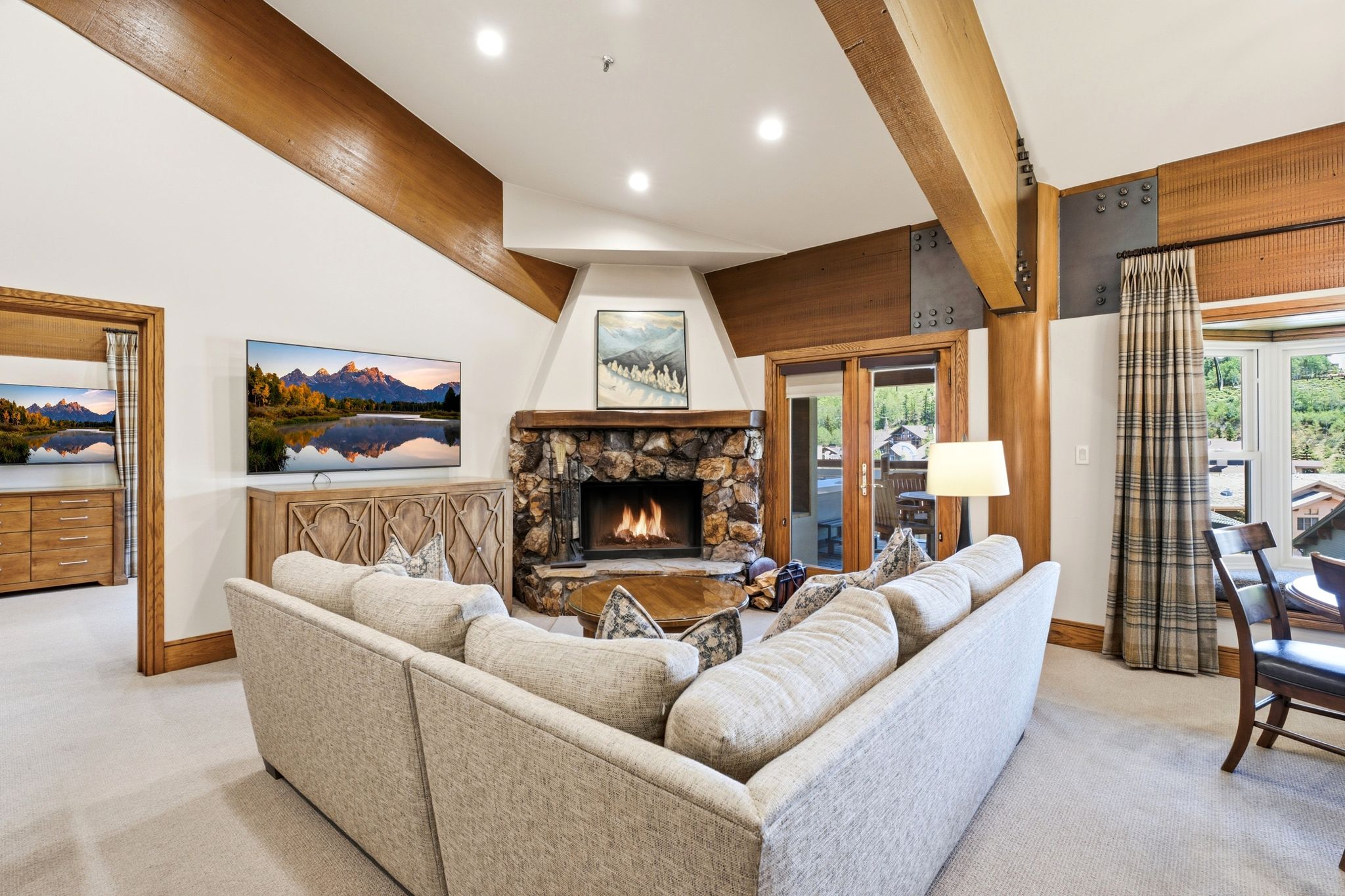 Living area featuring a stone-clad fireplace, exposed wood beams, and a window bay