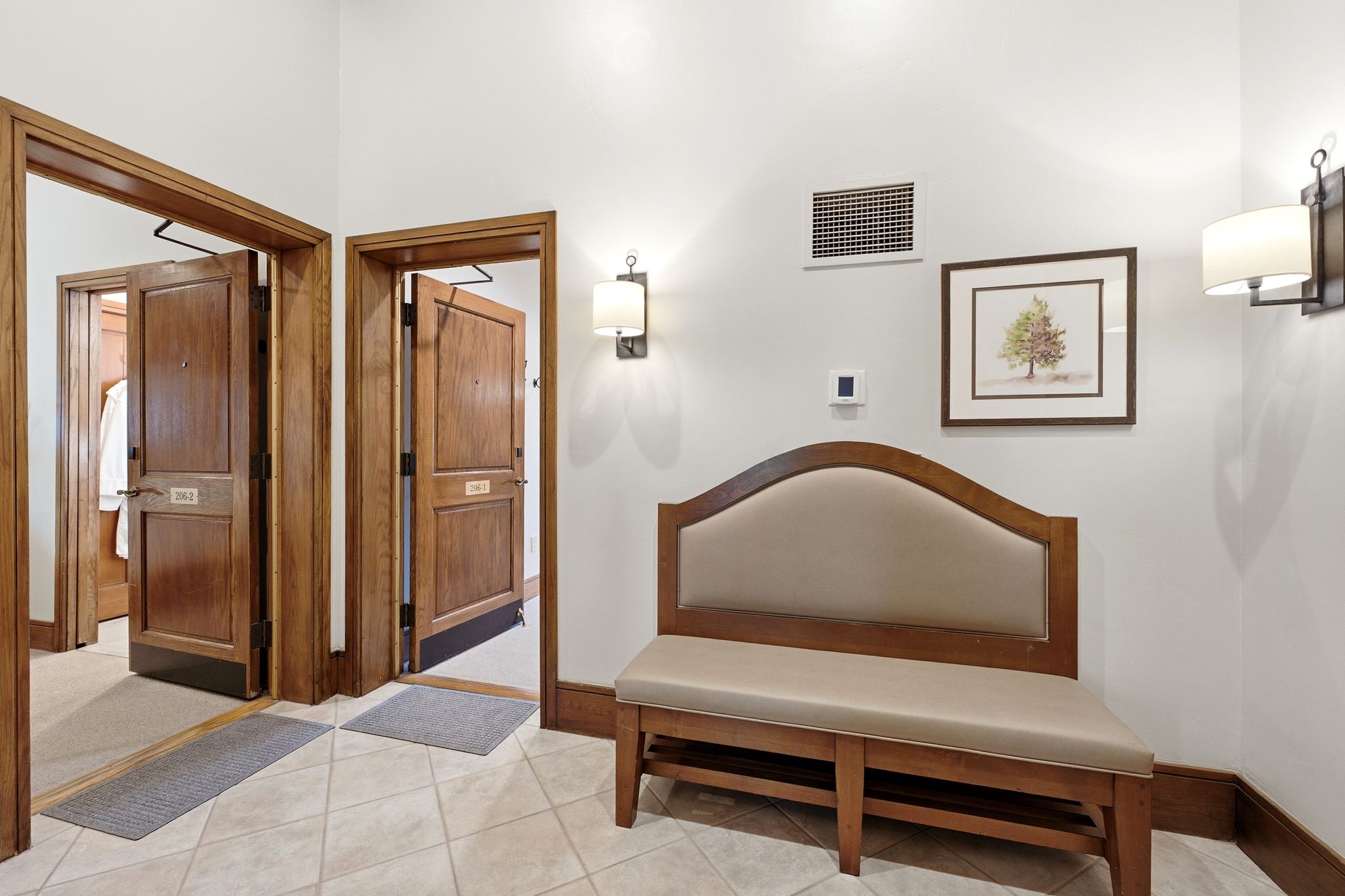 Entryway featuring warm wood-paneled doors, neutral tile flooring, and wall-mounted sconces