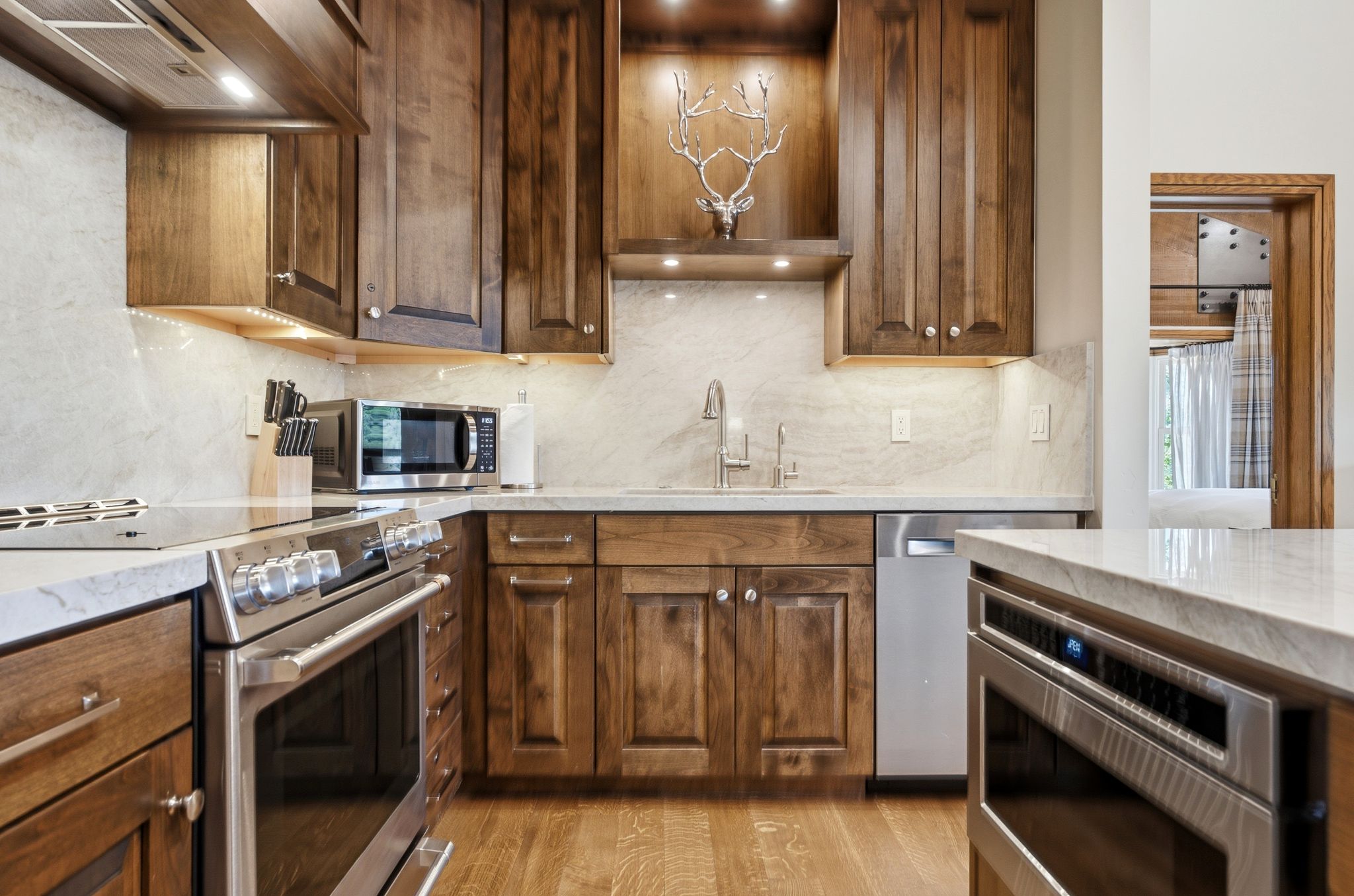 Kitchen featuring rich wood cabinetry, light-toned countertops, stainless steel appliances, a built-in microwave, and wood-finish flooring