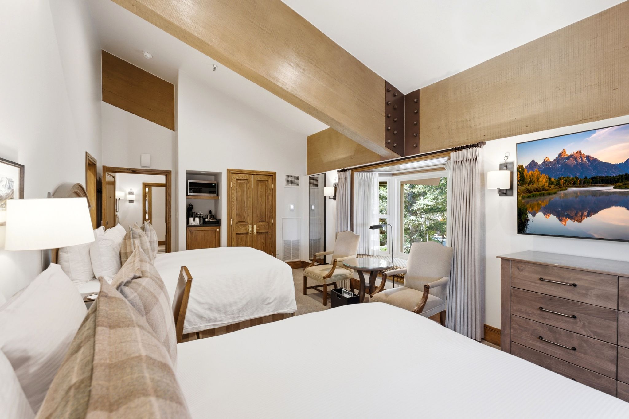 Vaulted ceilings with exposed wood beams define this space, featuring a built-in refreshment area with microwave, double wood-paneled doors, and a seating area with outdoor views