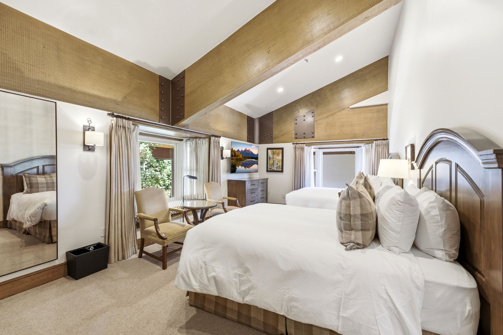 Vaulted ceiling with exposed wood beams, soft carpet flooring, and two distinct sleeping areas