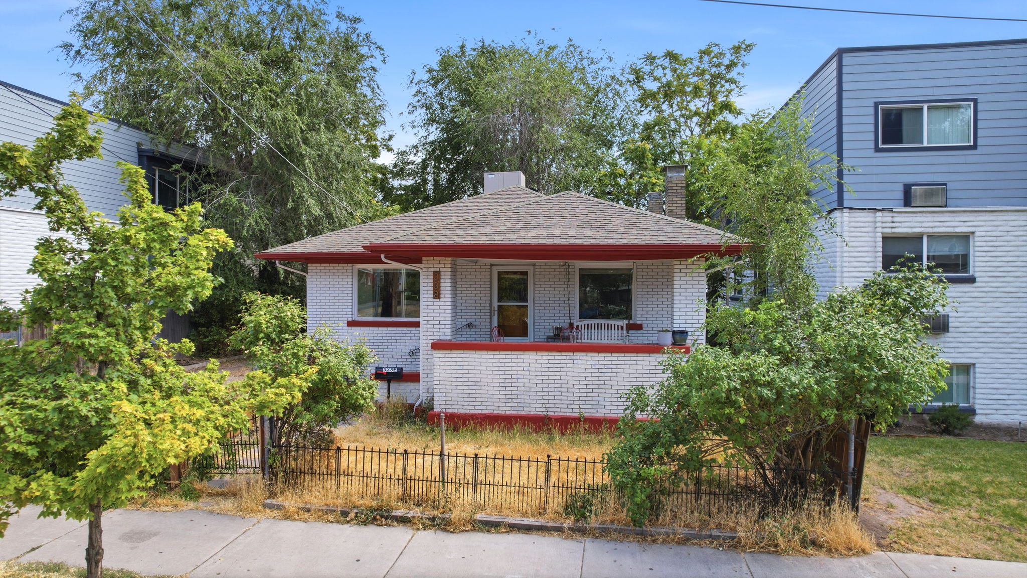 White brick exterior with a red-trimmed roofline, covered front porch, and a perimeter fence