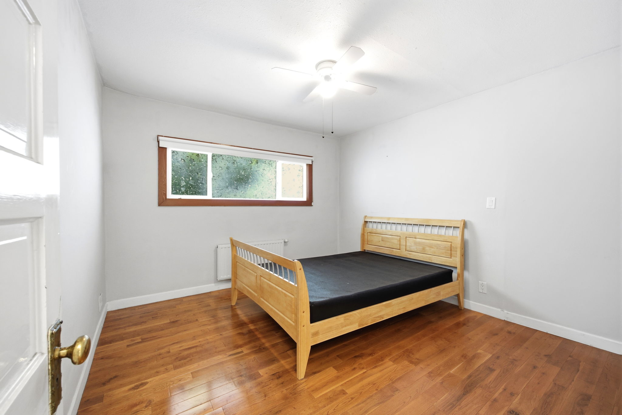 Room featuring wood-finish flooring, a window with wood trim, and a ceiling fan with integrated lighting