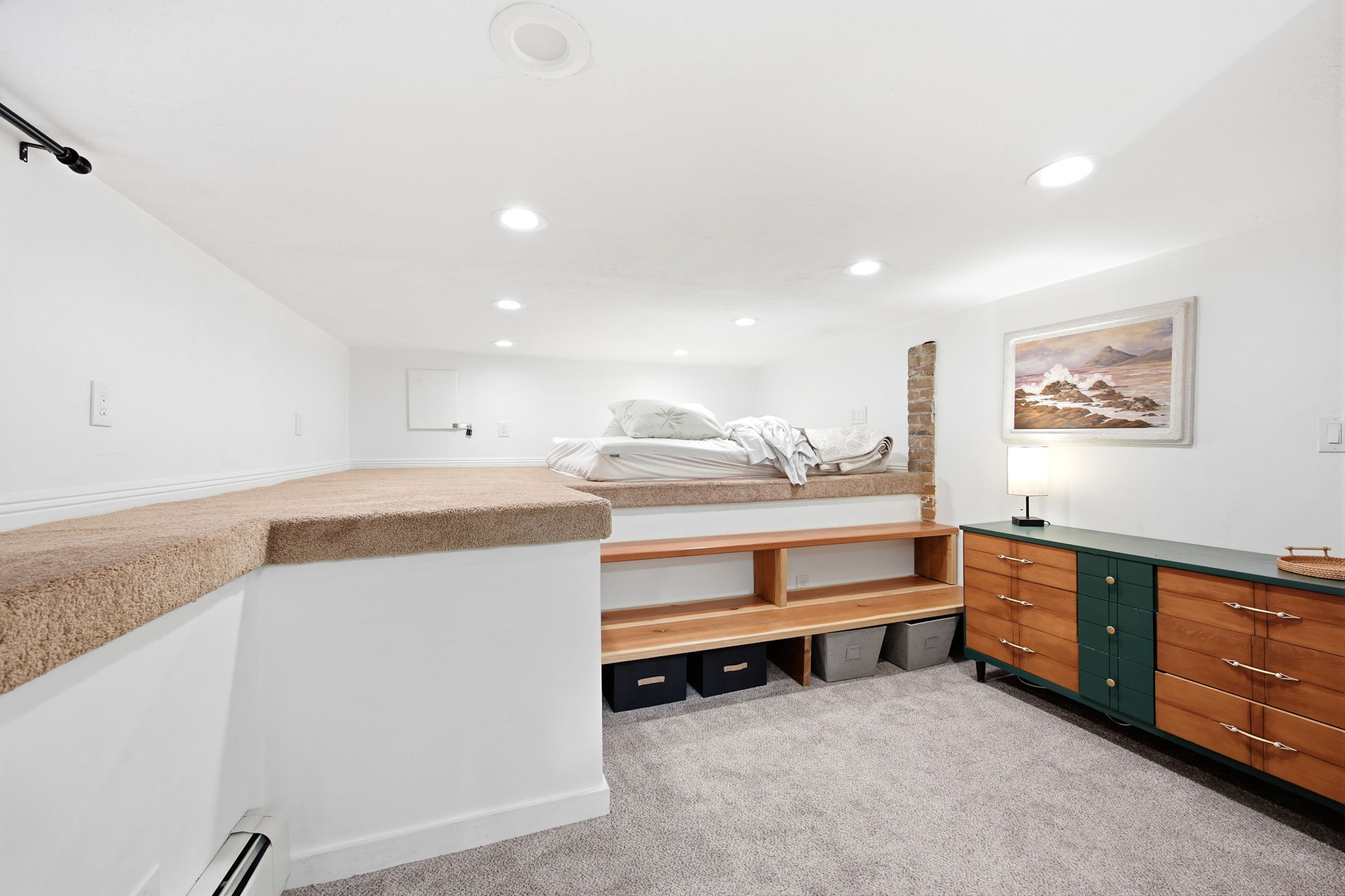 Carpeted raised platform area with integrated shelving, recessed lighting, and a neutral color palette