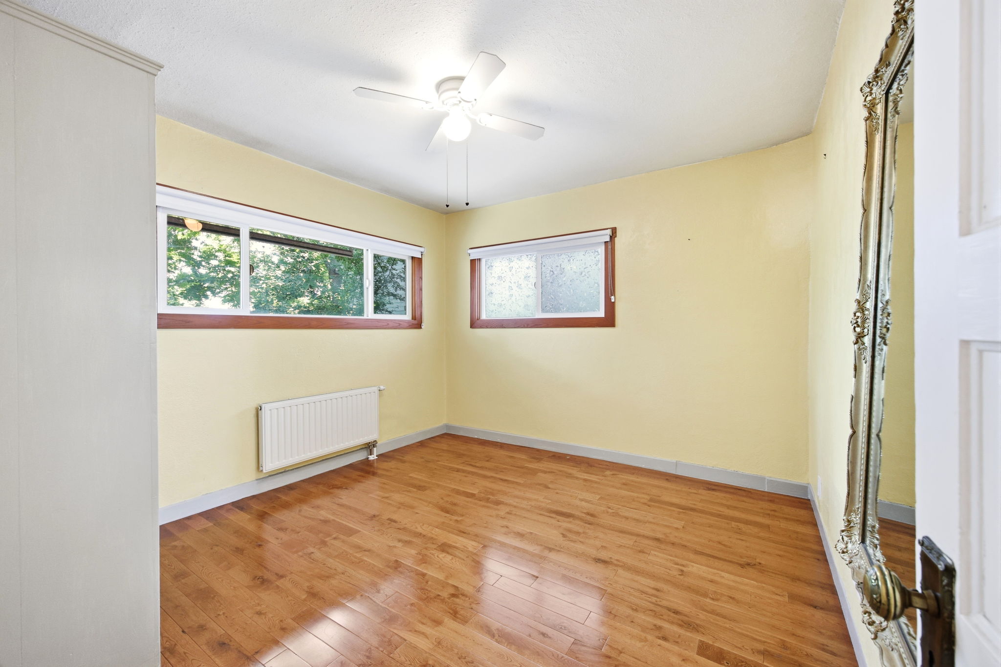 Interior space featuring wood-finish flooring, two windows with wood trim, and a ceiling fan