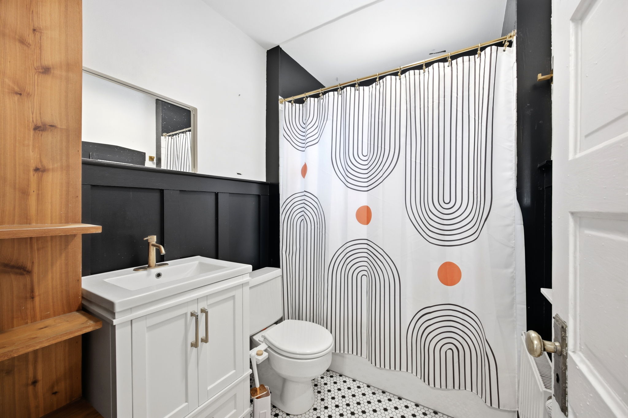 Contemporary bathroom featuring hexagonal mosaic floor tiling, a white vanity with gold-tone hardware and faucet, a rectangular mirror, and black wainscoting