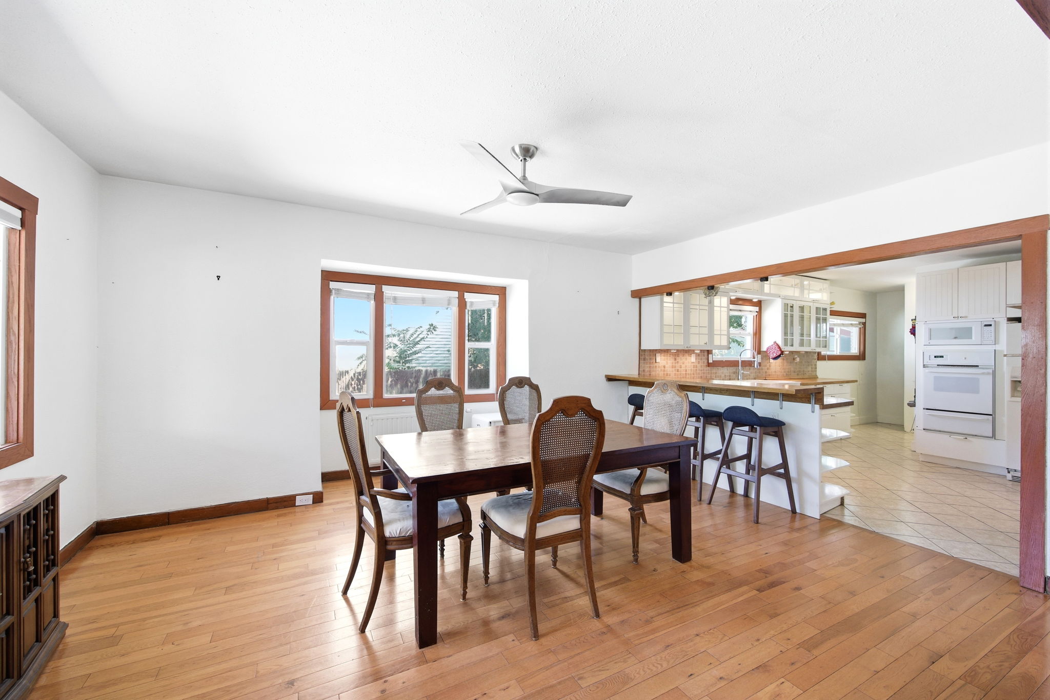 Open-concept dining area featuring wood-finish flooring, a modern ceiling fan, and multiple windows with wood trim