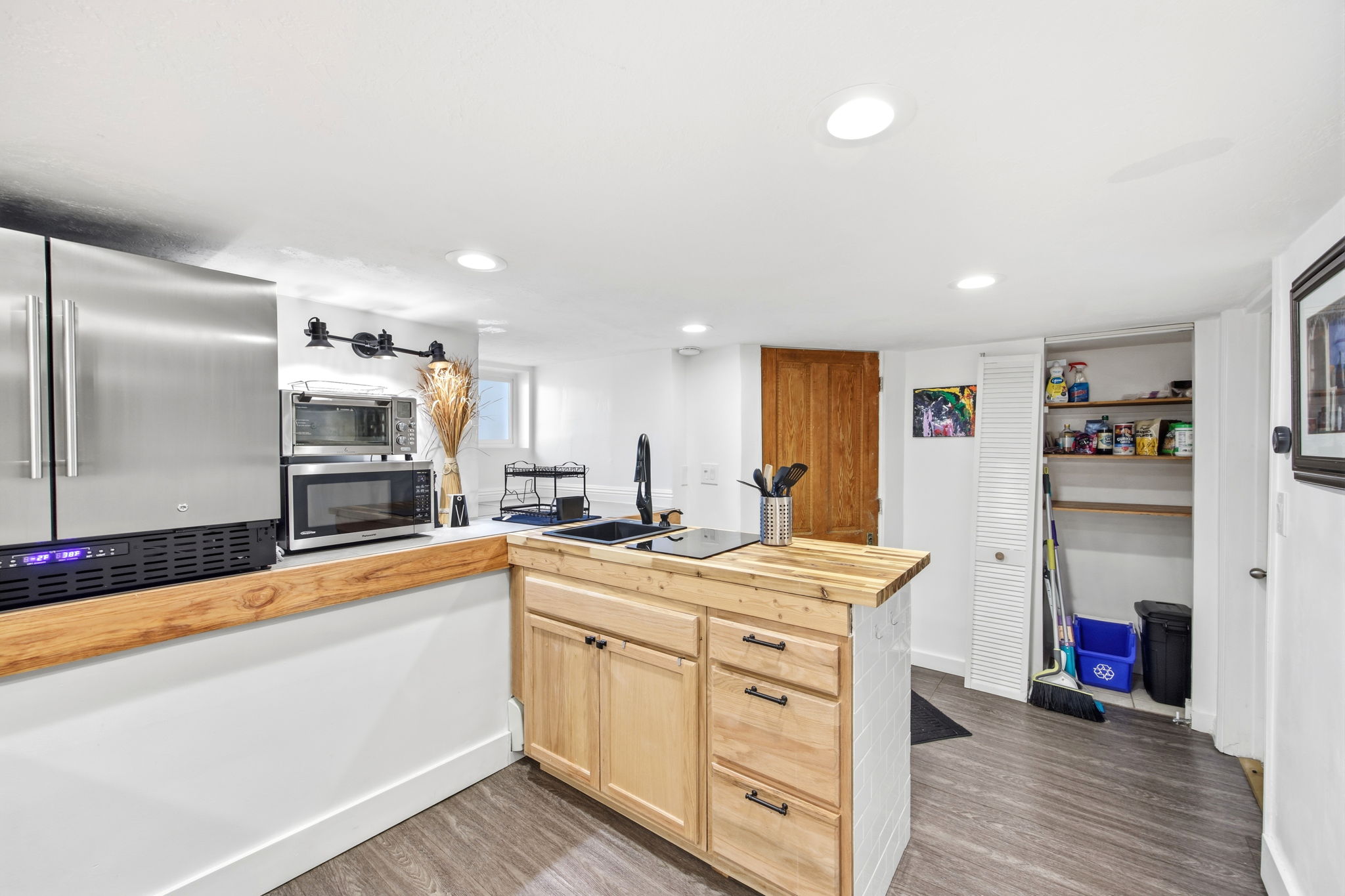 Kitchenette featuring stainless steel refrigerator, wood-finish flooring, recessed lighting, and a wood countertop island with built-in cabinetry and a black sink