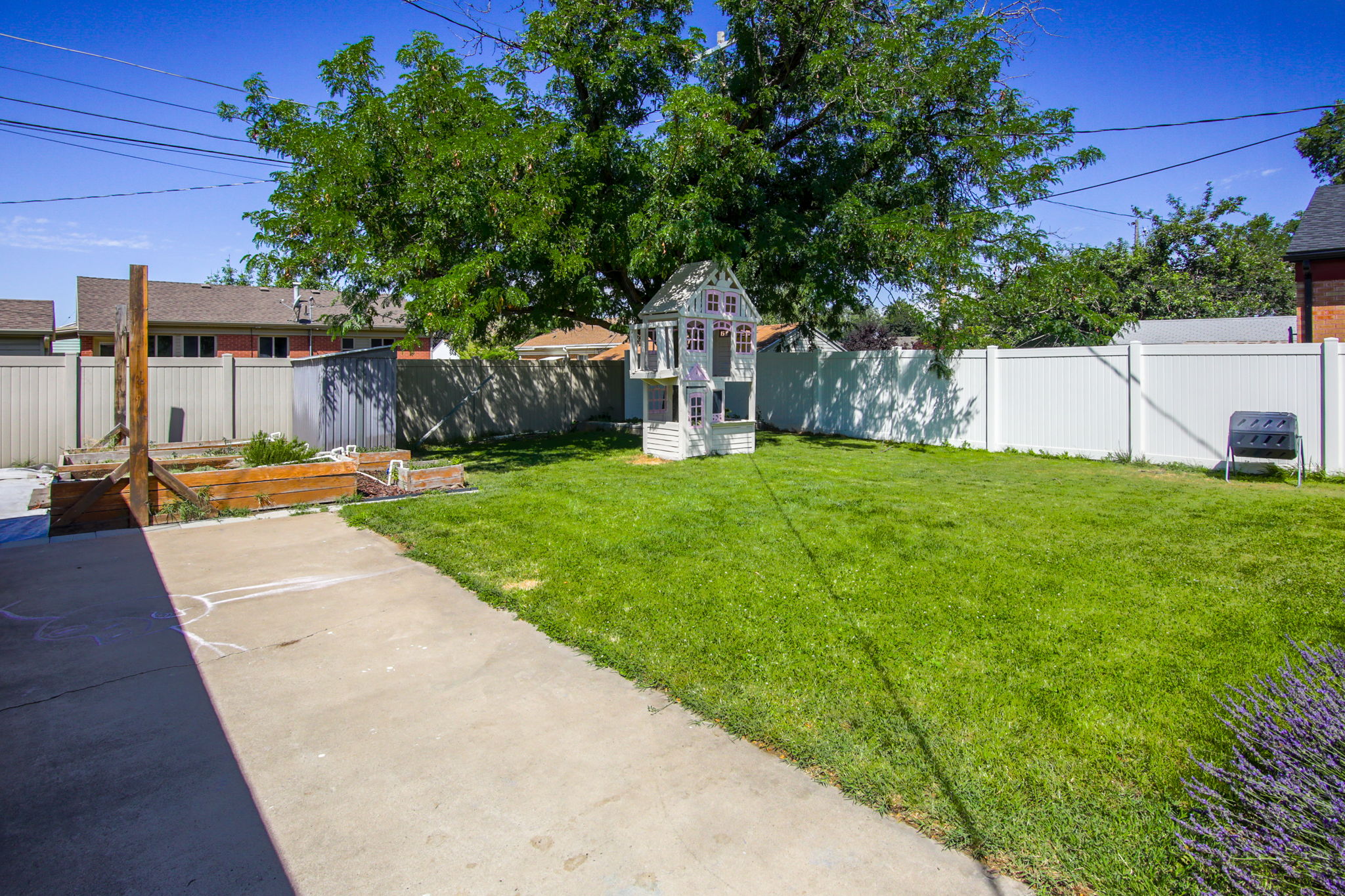 Expansive backyard featuring a large grass lawn, mature tree, raised garden beds, and substantial fencing