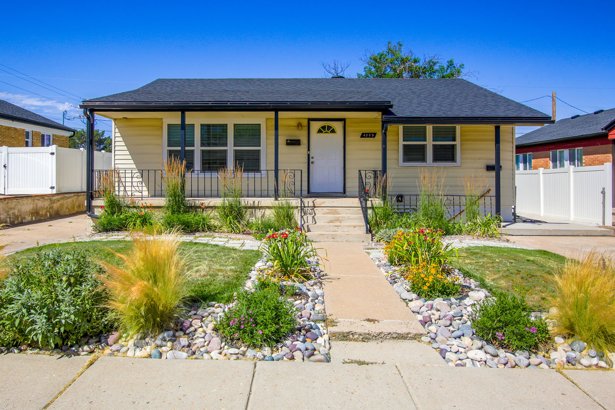 Front exterior featuring light yellow siding, a covered porch with black railing, a dark shingled roof, a white entry door, and a concrete pathway through the front yard