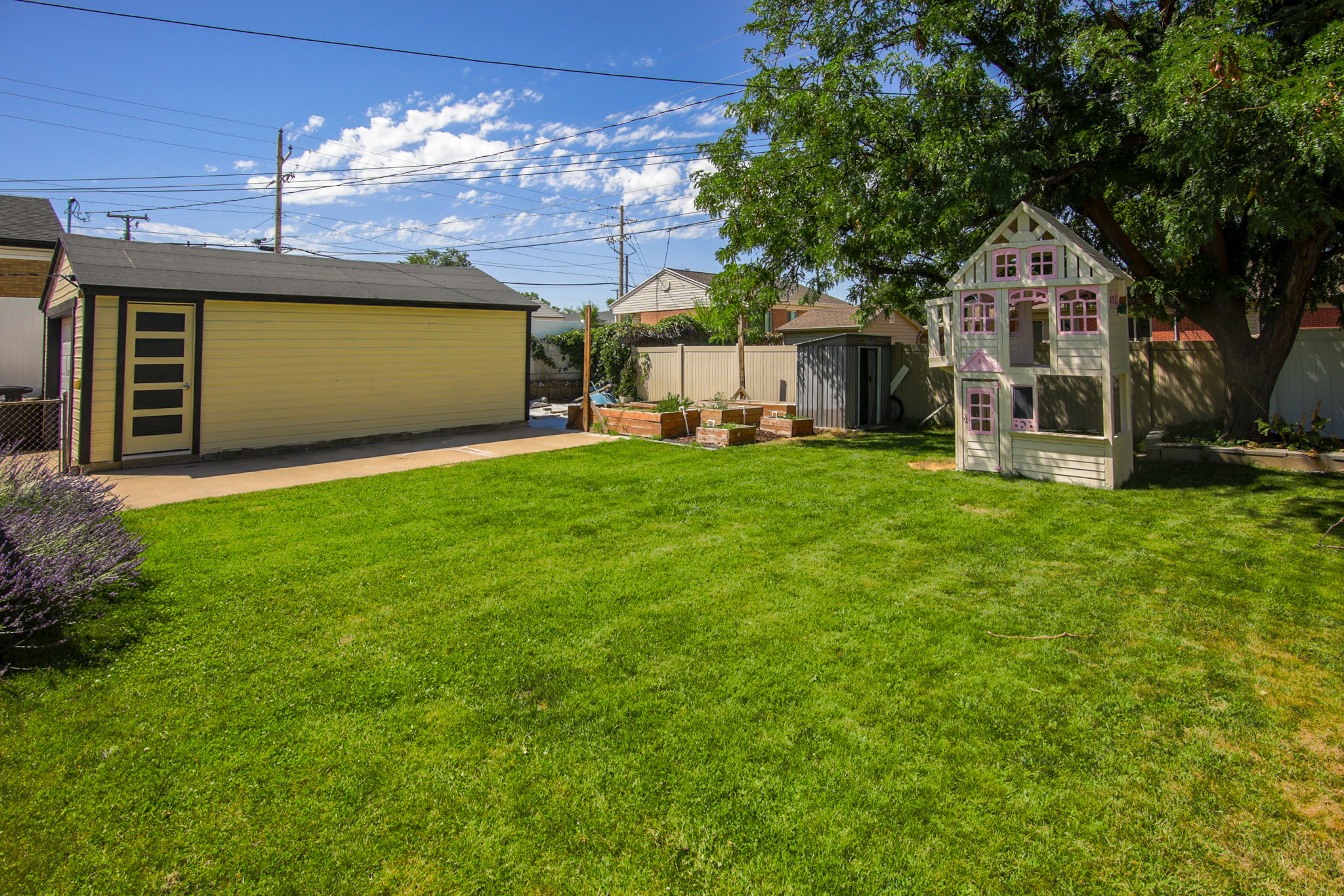 Expansive grassy yard with a detached garage featuring a contemporary side entry door, mature perimeter trees, and a concrete pathway