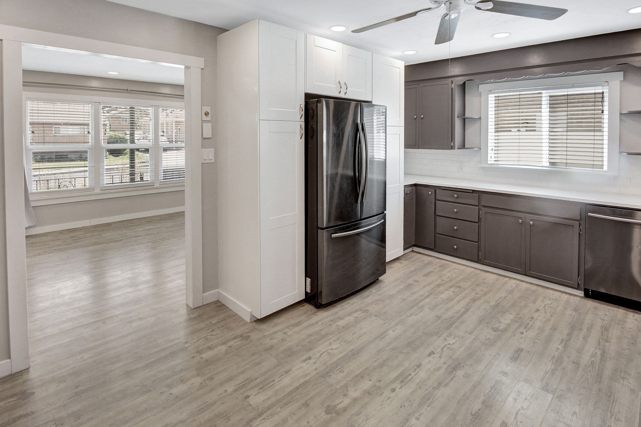 Modern kitchen featuring wood-finish flooring, two-tone cabinetry with white upper and dark lower units, stainless steel appliances, and a white countertop