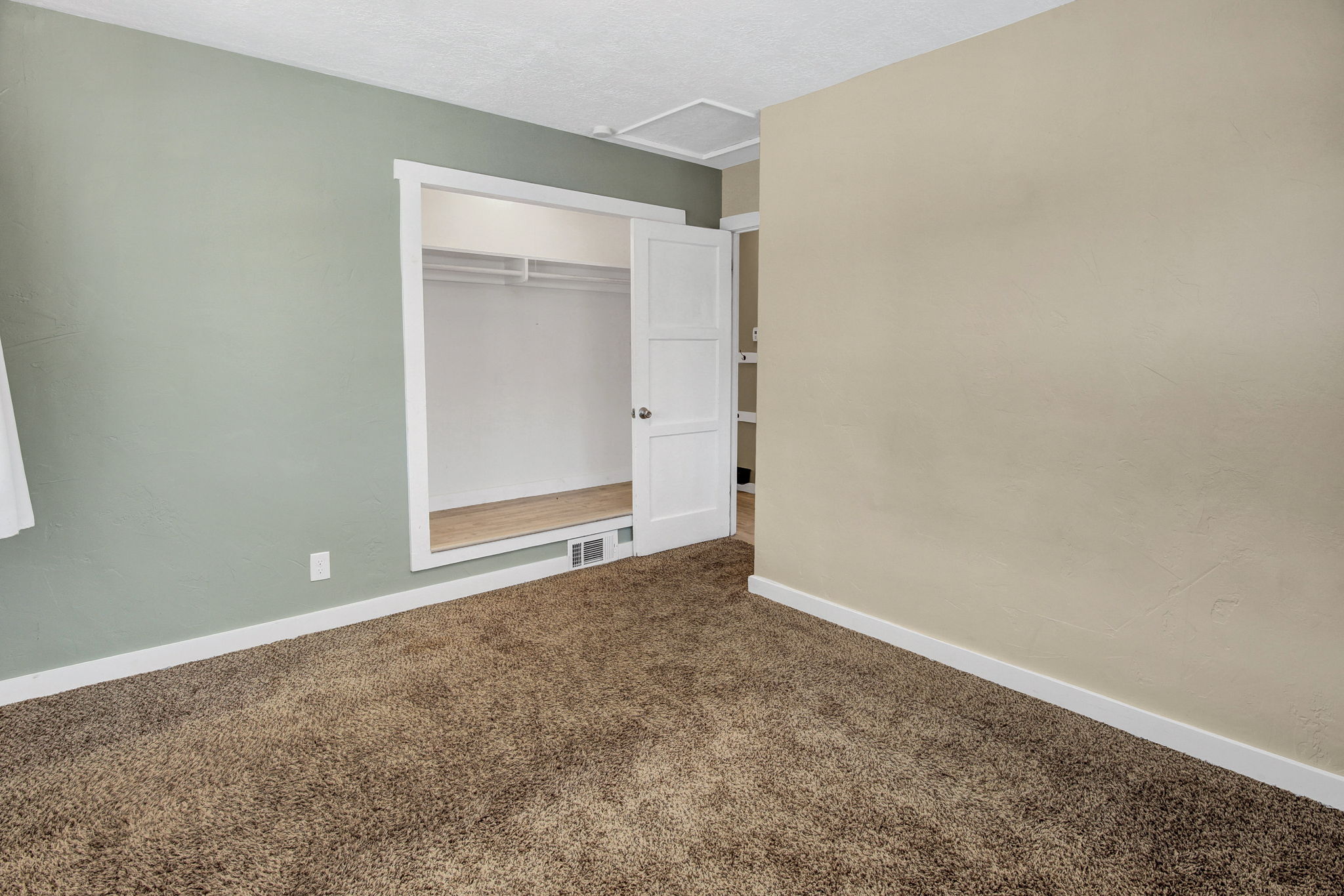 Carpeted room featuring a built-in closet with wood-finish flooring and bi-fold doors, complemented by white baseboards