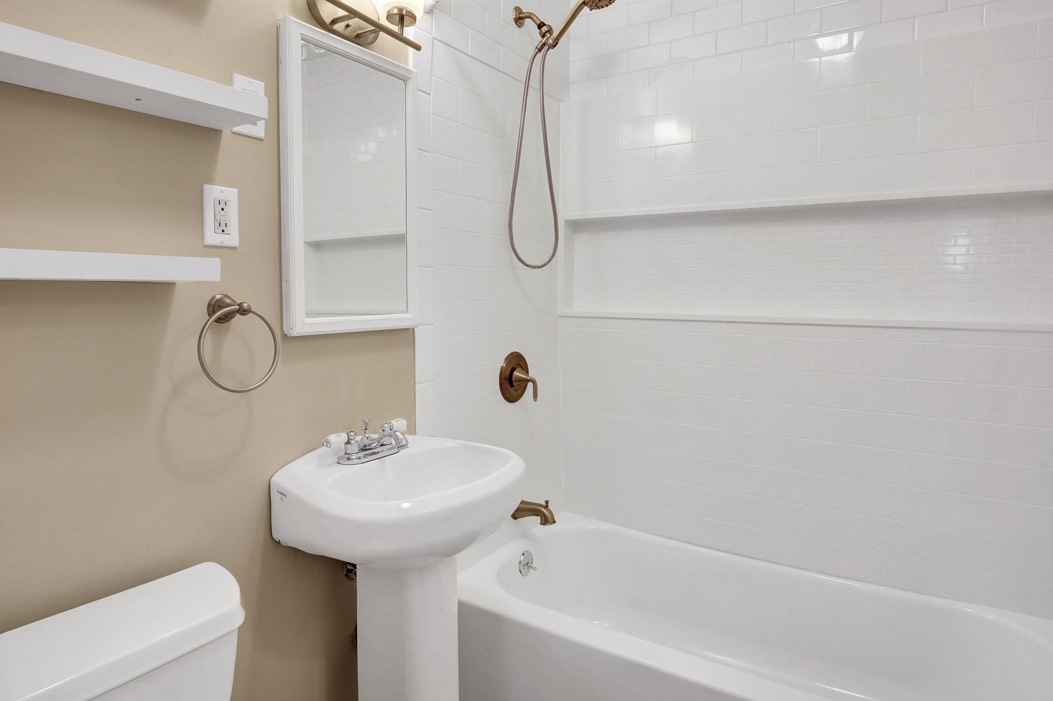 Bathroom featuring white subway tile surround with integrated niche, white pedestal sink, and bronze shower fixtures