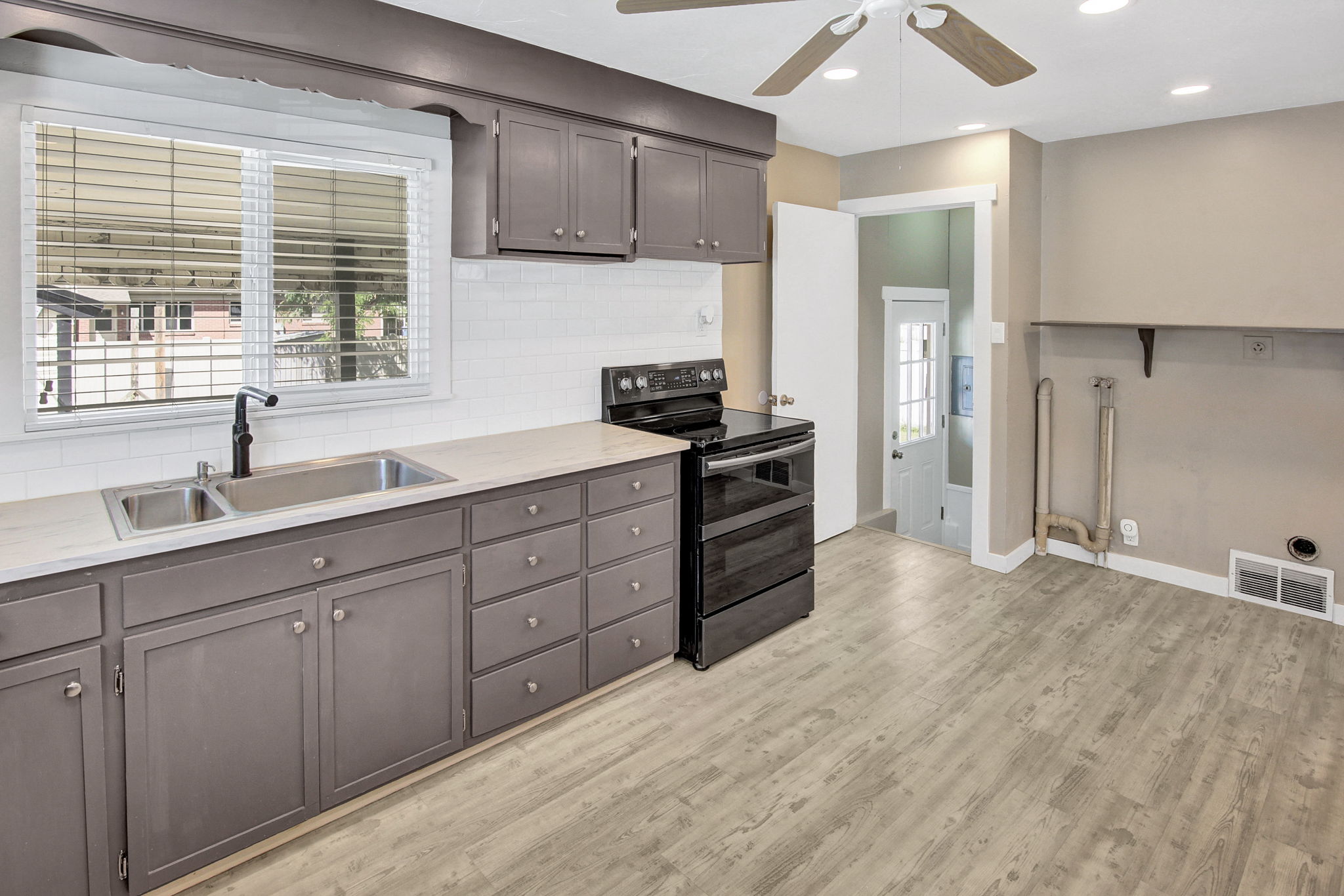 Kitchen featuring gray cabinetry, a double basin stainless steel sink, a black electric range, white subway tile backsplash, and wood-finish flooring