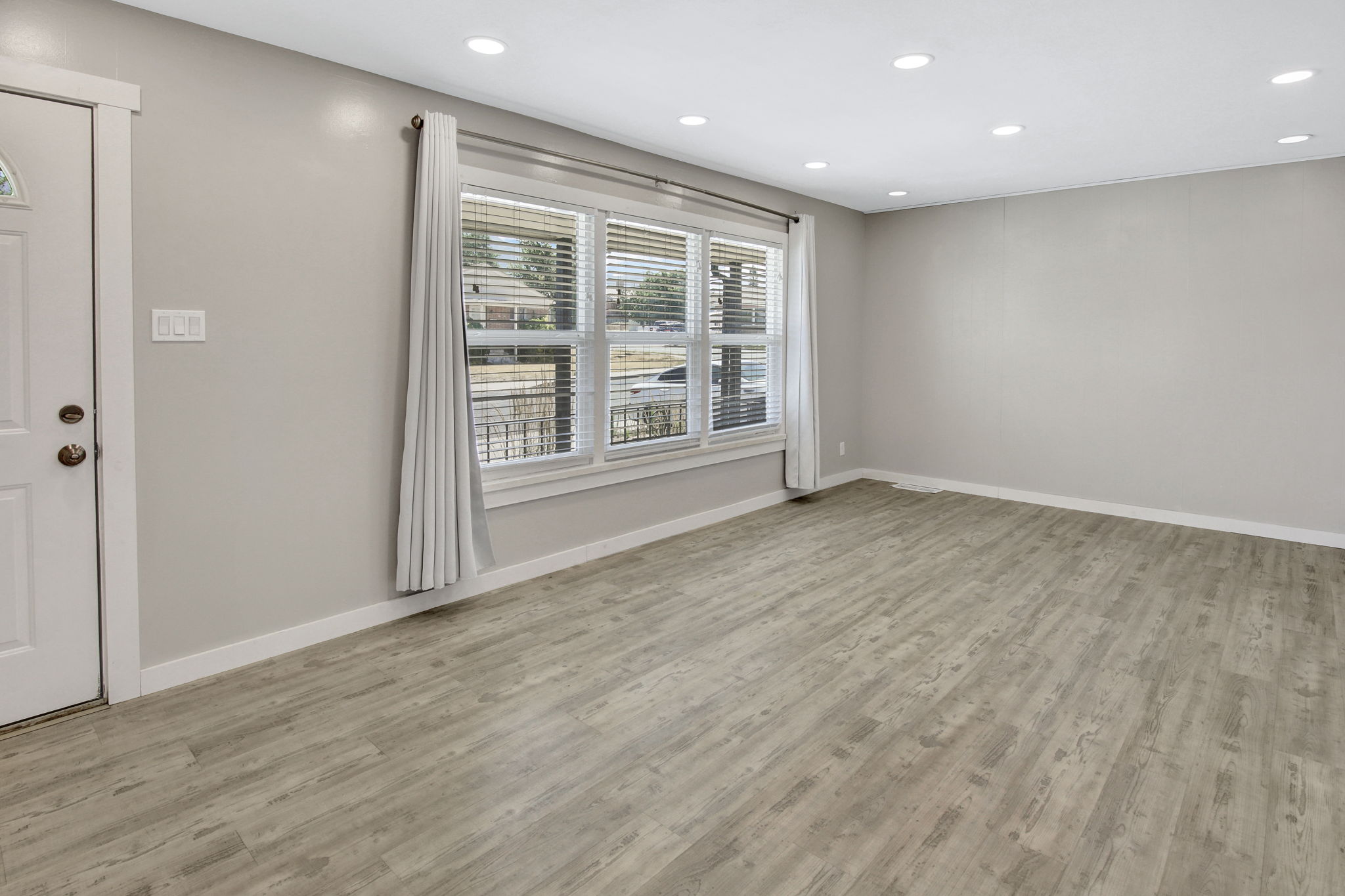 Spacious room featuring wood-finish flooring, recessed lighting, and a large window with blinds