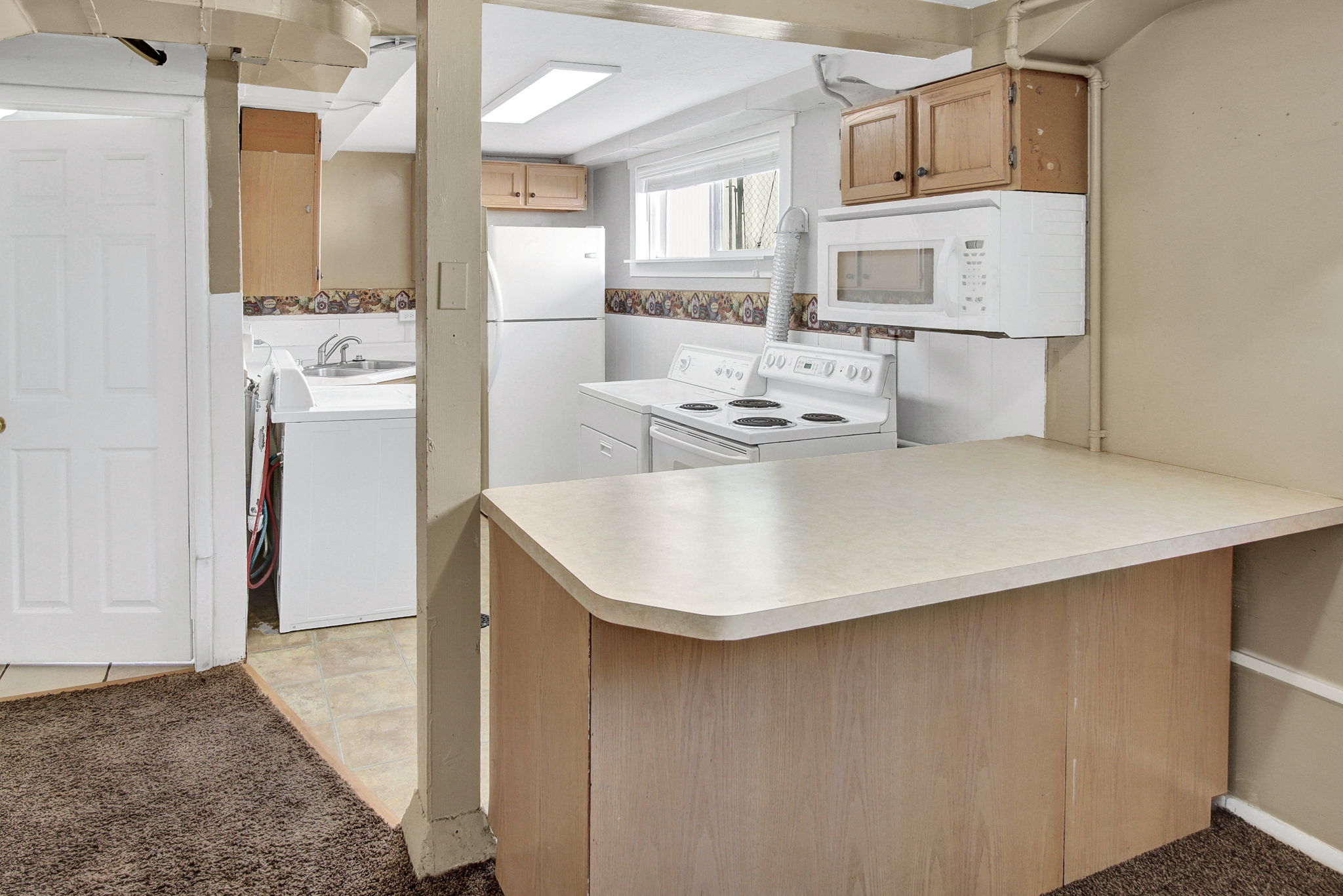 Kitchenette featuring an integrated breakfast bar, white appliances, and wood-finish cabinetry