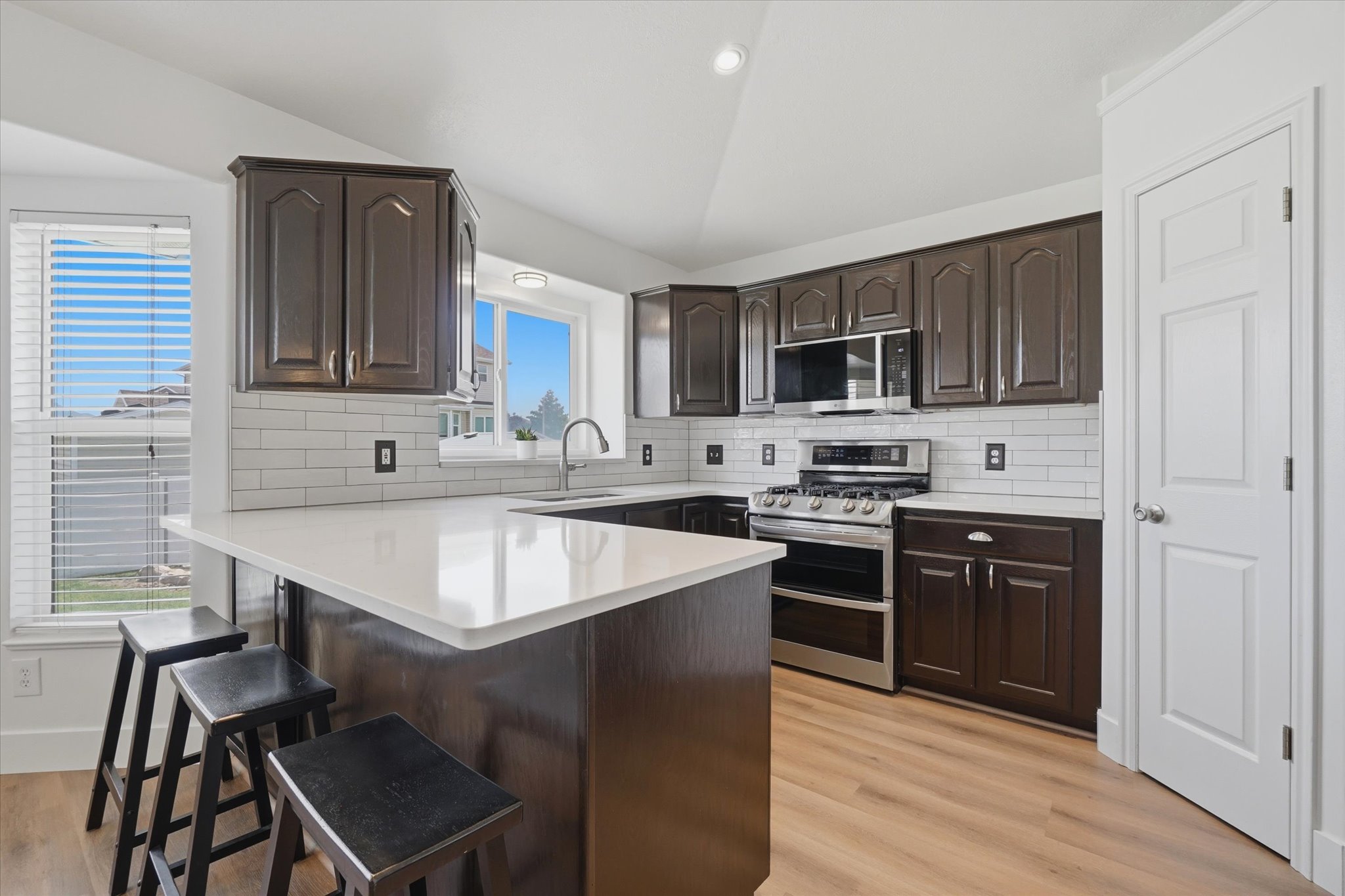Modern kitchen featuring dark wood cabinetry, white subway tile backsplash, LVP flooring, and quartzite
