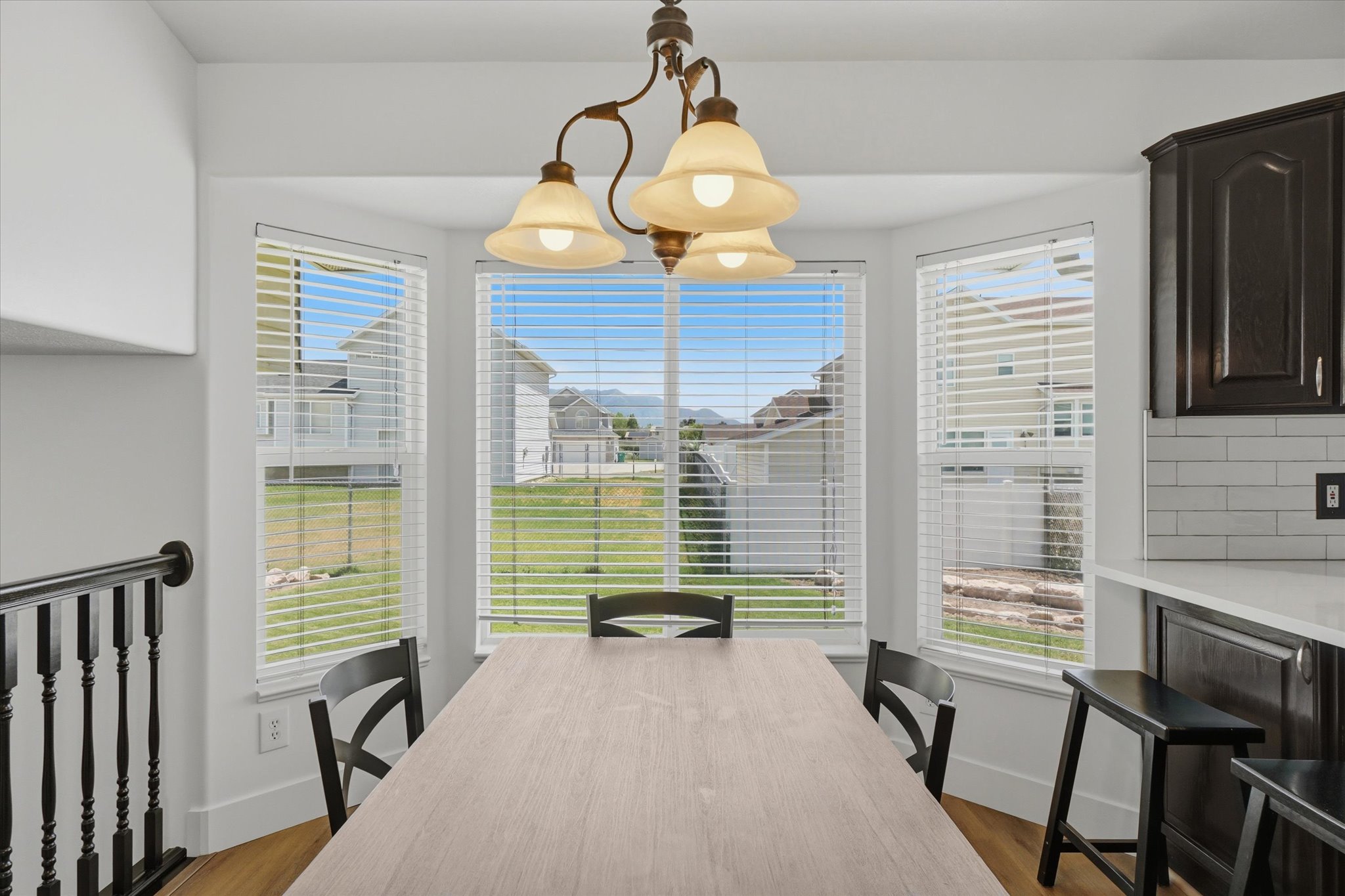 Bay window dining area featuring a three-light chandelier, wood-finish flooring, and white window blinds