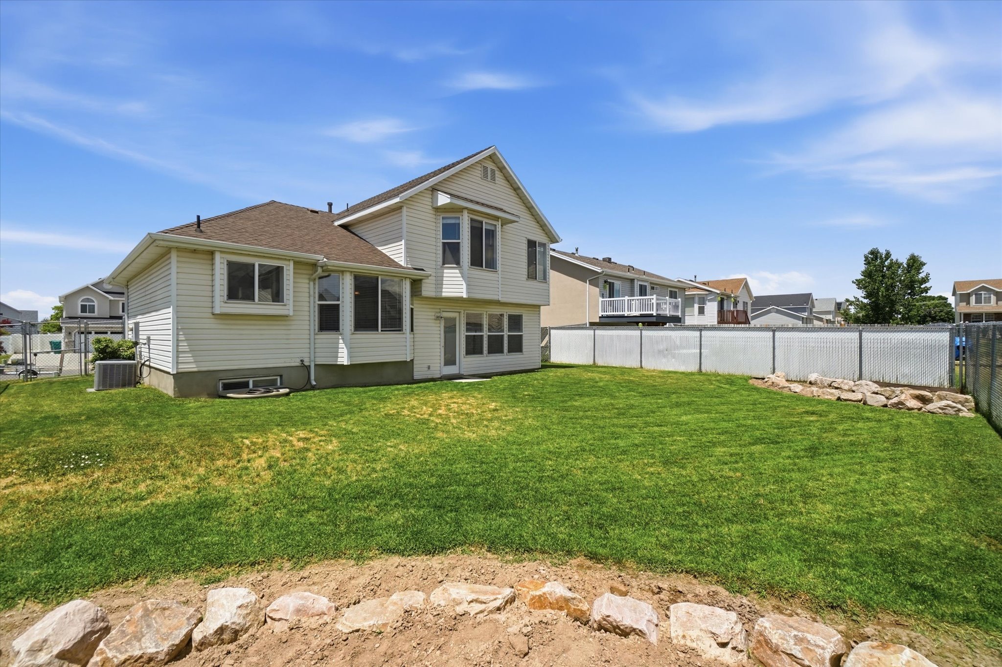 Expansive backyard featuring a manicured lawn, white privacy fencing, and a decorative rock border