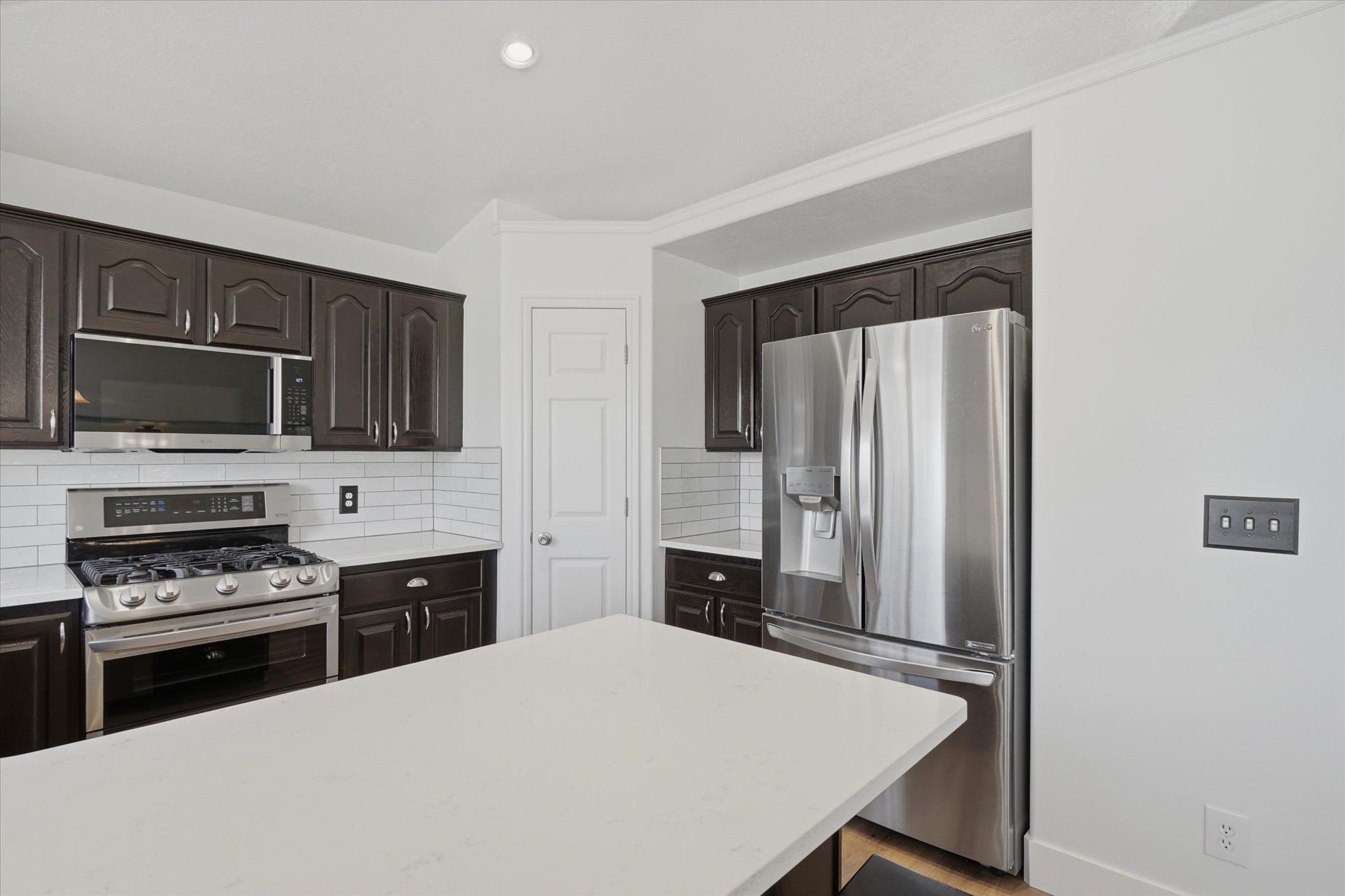 Kitchen featuring dark wood cabinetry, stainless steel appliances, white subway tile backsplash, and light-toned countertops