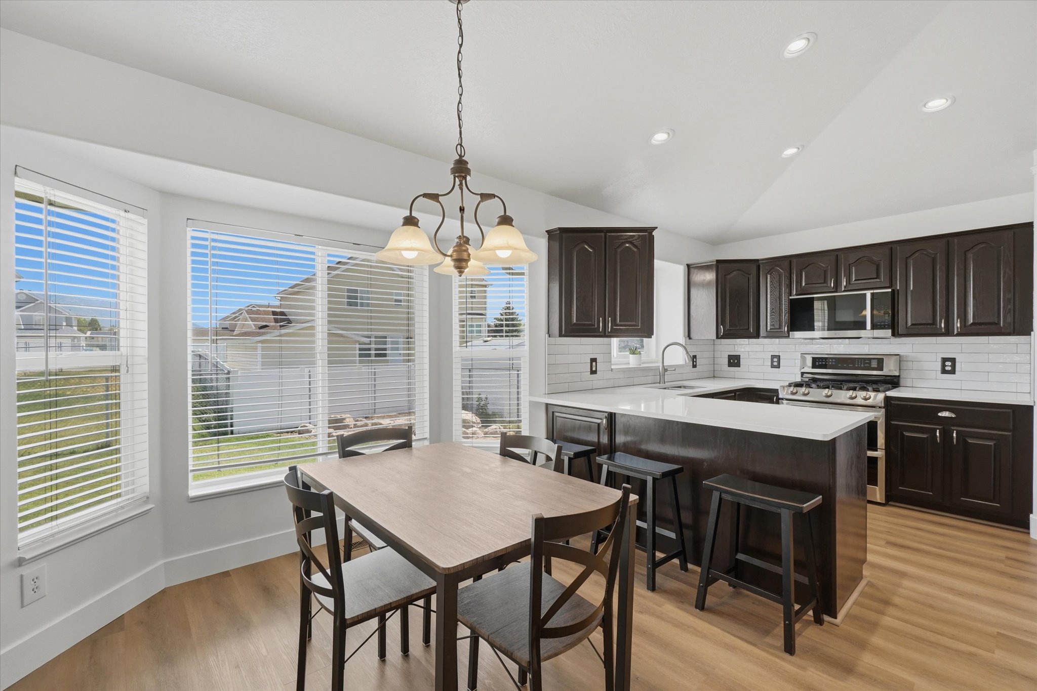 Open-concept kitchen and dining area featuring dark wood cabinetry, white subway tile backsplash, and light countertops