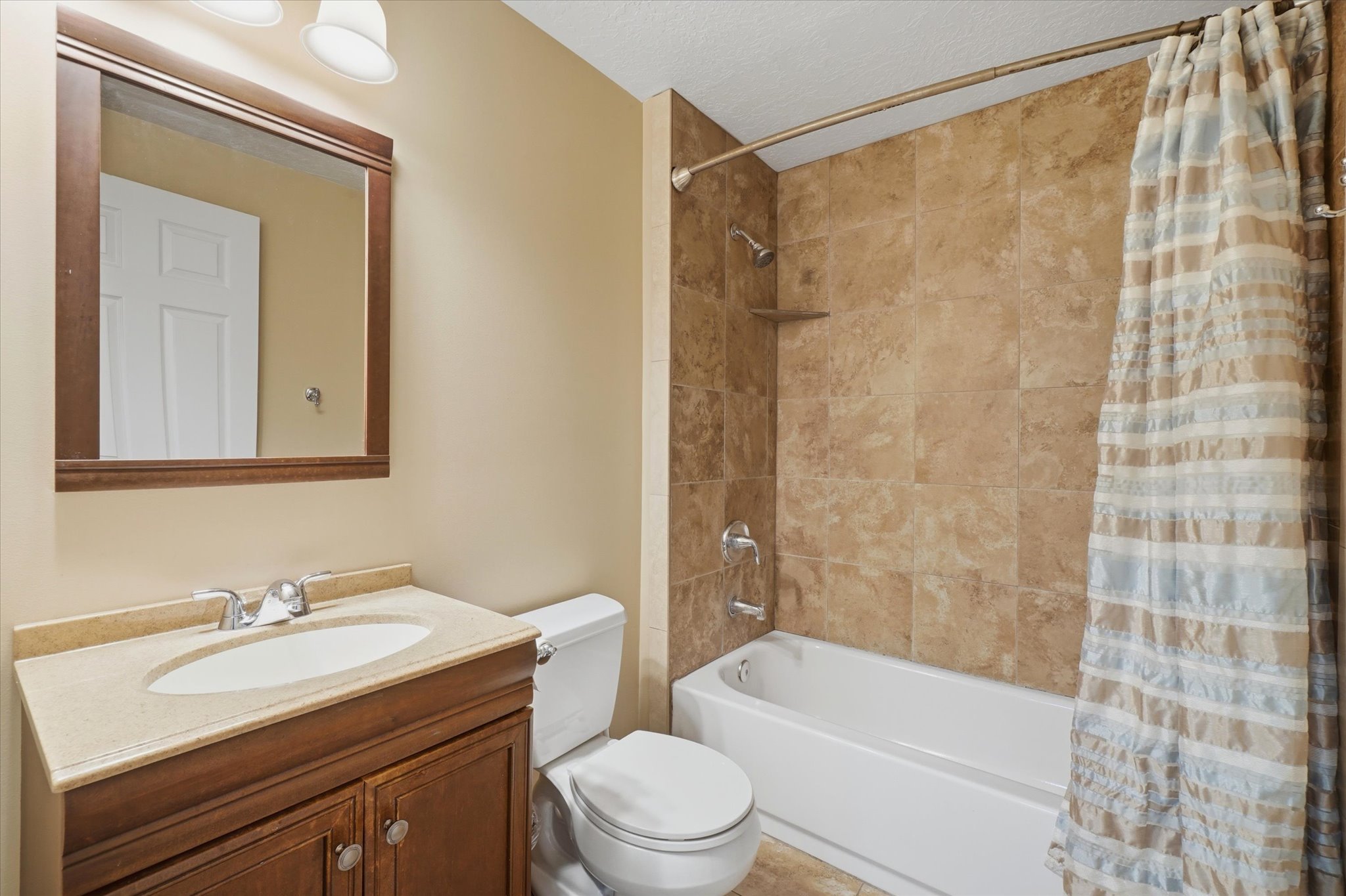 Bathroom featuring a vanity with a light-toned countertop, a wood-framed mirror, a toilet, a bathtub with a shower, and tiled shower walls