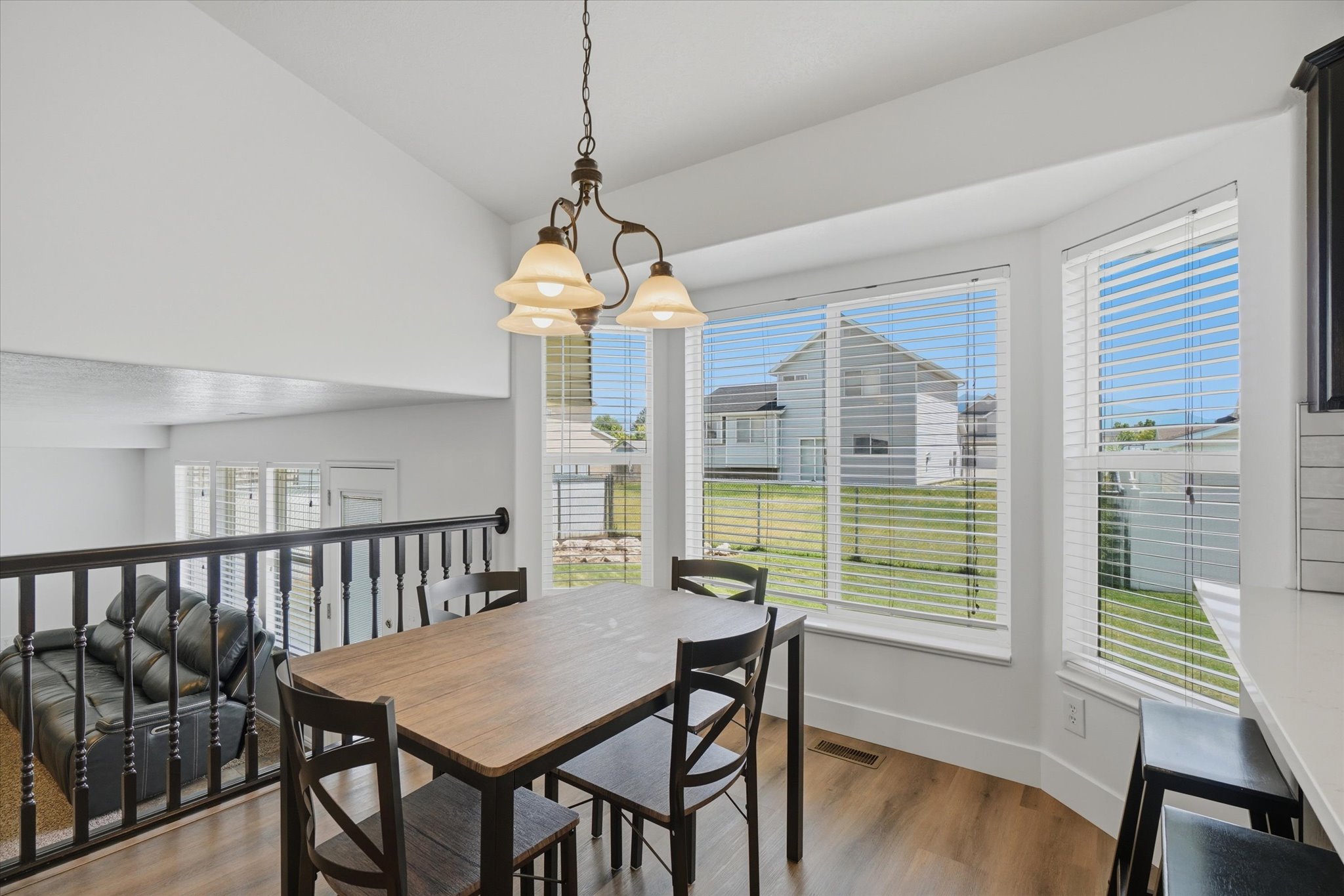 Bright dining area featuring a bay window, LVP flooring, and an open railing overlooking a lower level