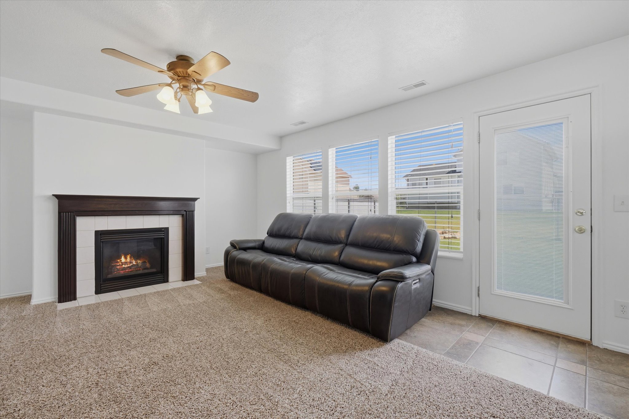 Living area featuring a gas fireplace with a dark wood mantel, tiled surround, and a ceiling fan