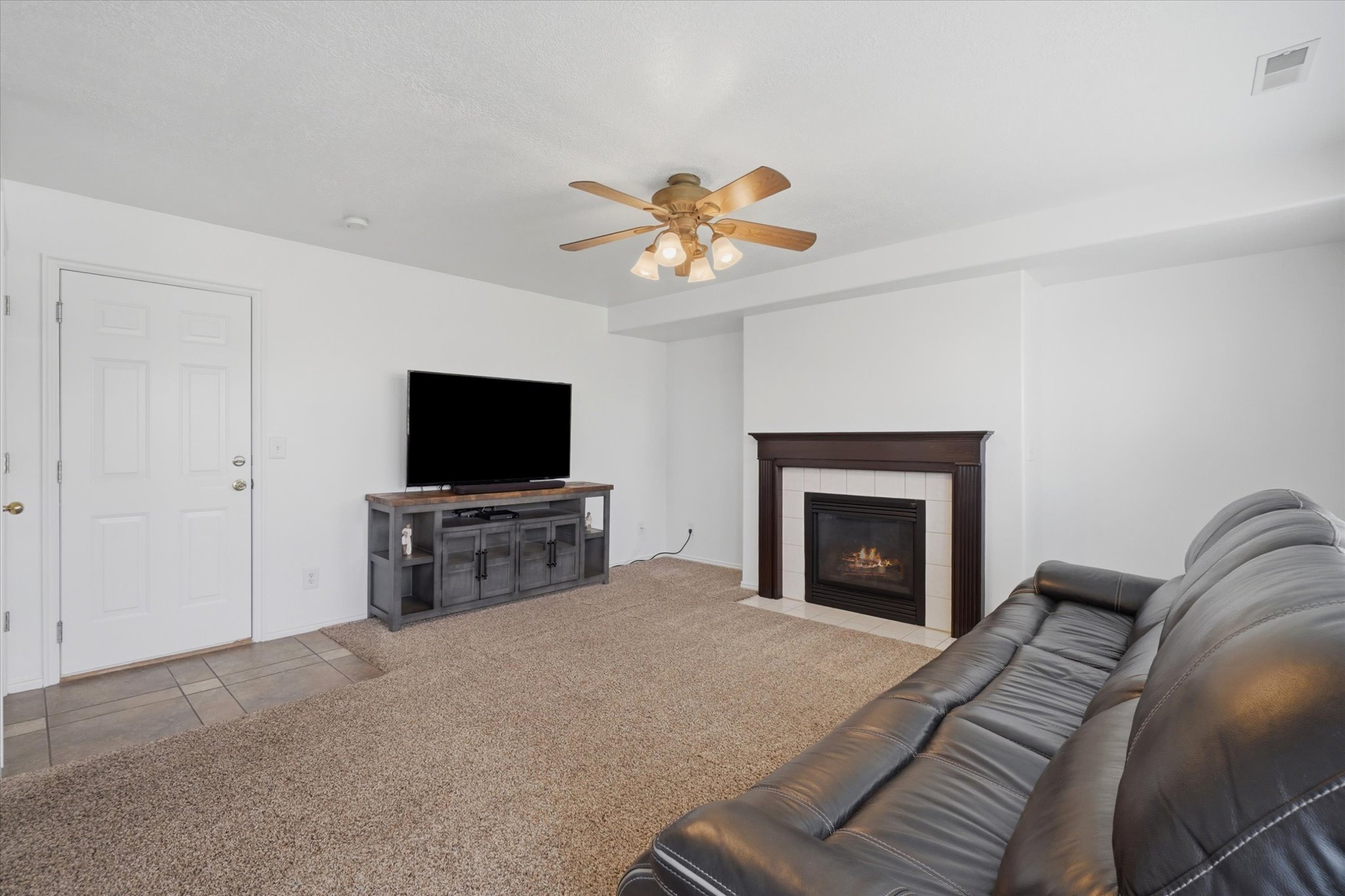 Living area featuring a gas fireplace with a dark wood mantel and white surround, complemented by a ceiling fan with integrated lighting, and carpet flooring