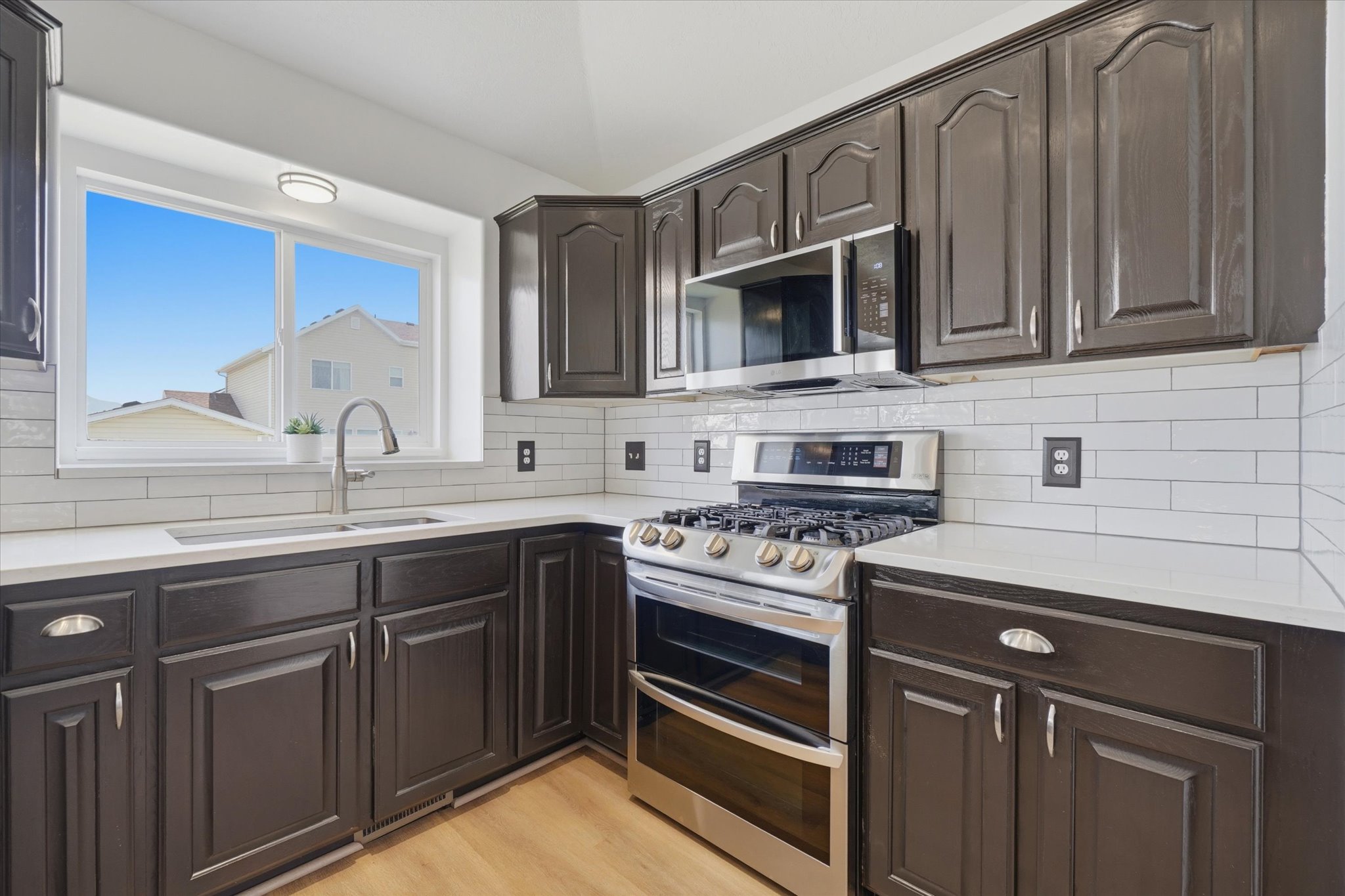 Contemporary kitchen featuring dark cabinetry, white countertops, stainless steel appliances, and a subway tile backsplash