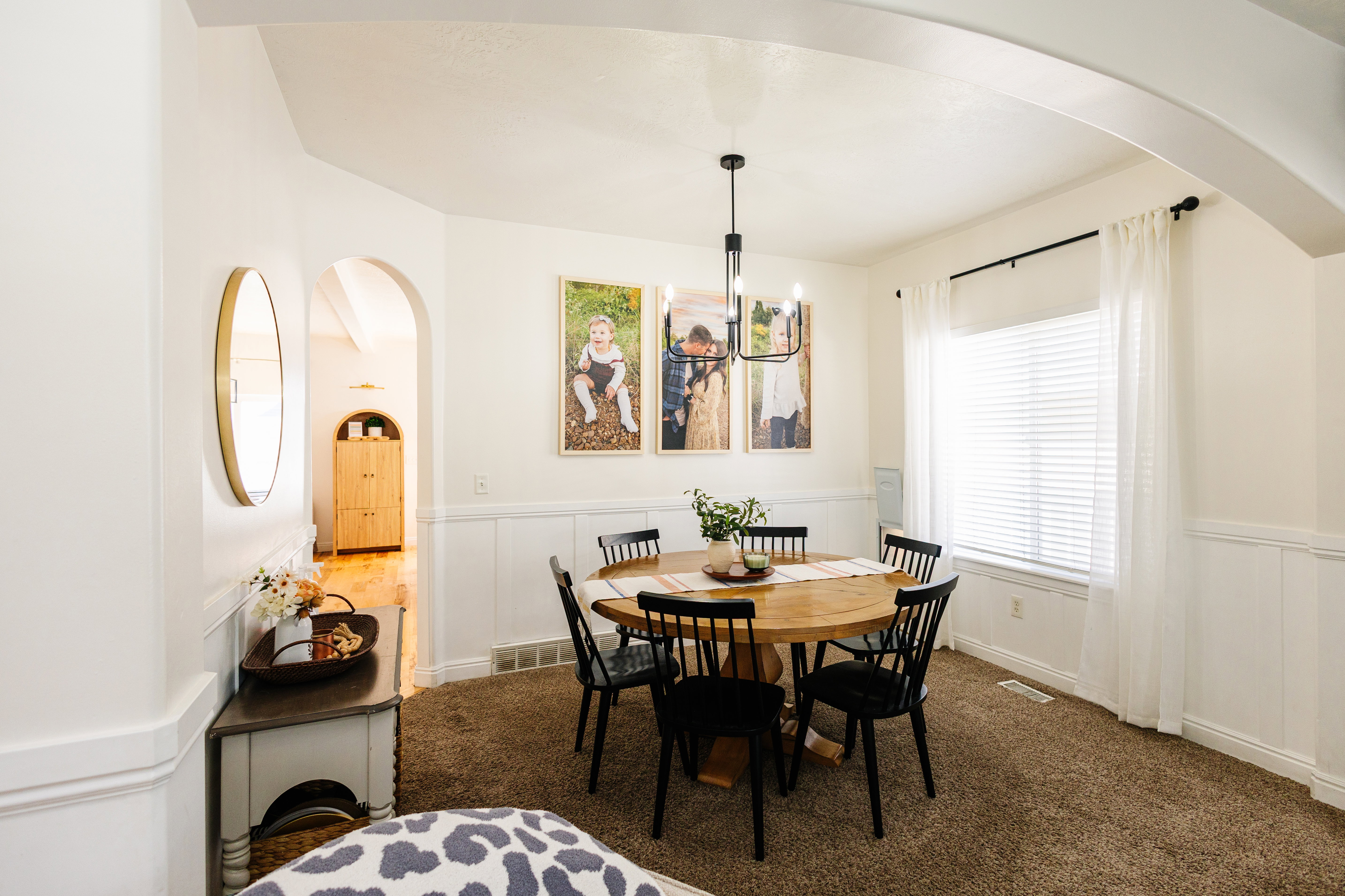 Dining area featuring wainscoting, arched doorways, a contemporary chandelier, and a large window with blinds and sheer curtains