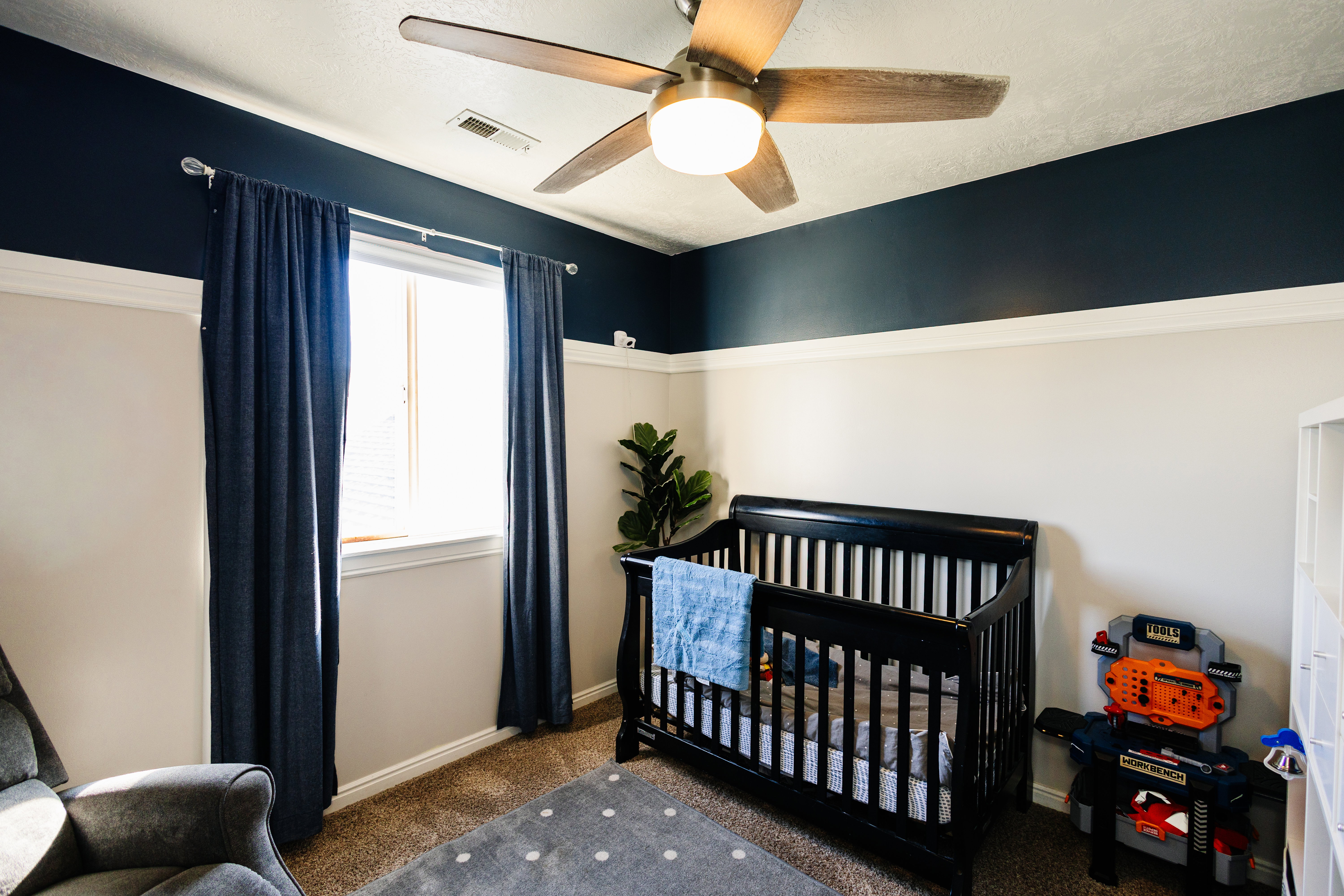 Bedroom featuring a single window with blinds, carpet flooring, a ceiling fan with integrated lighting, and a two-tone wall treatment with a white base and a dark accent band