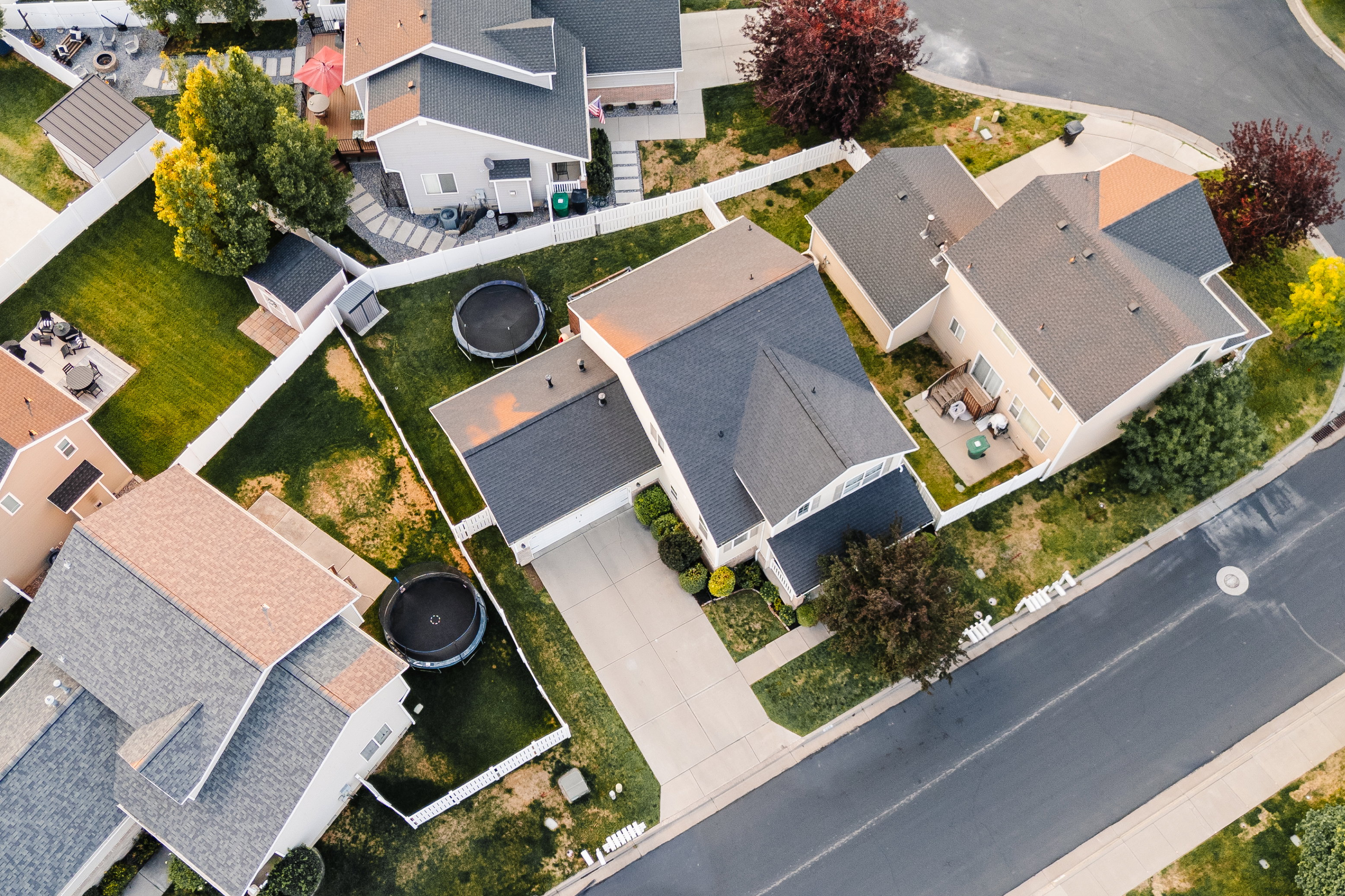 Aerial perspective showcasing a residential property with a dark shingle roof, a concrete driveway, and a white picket fence
