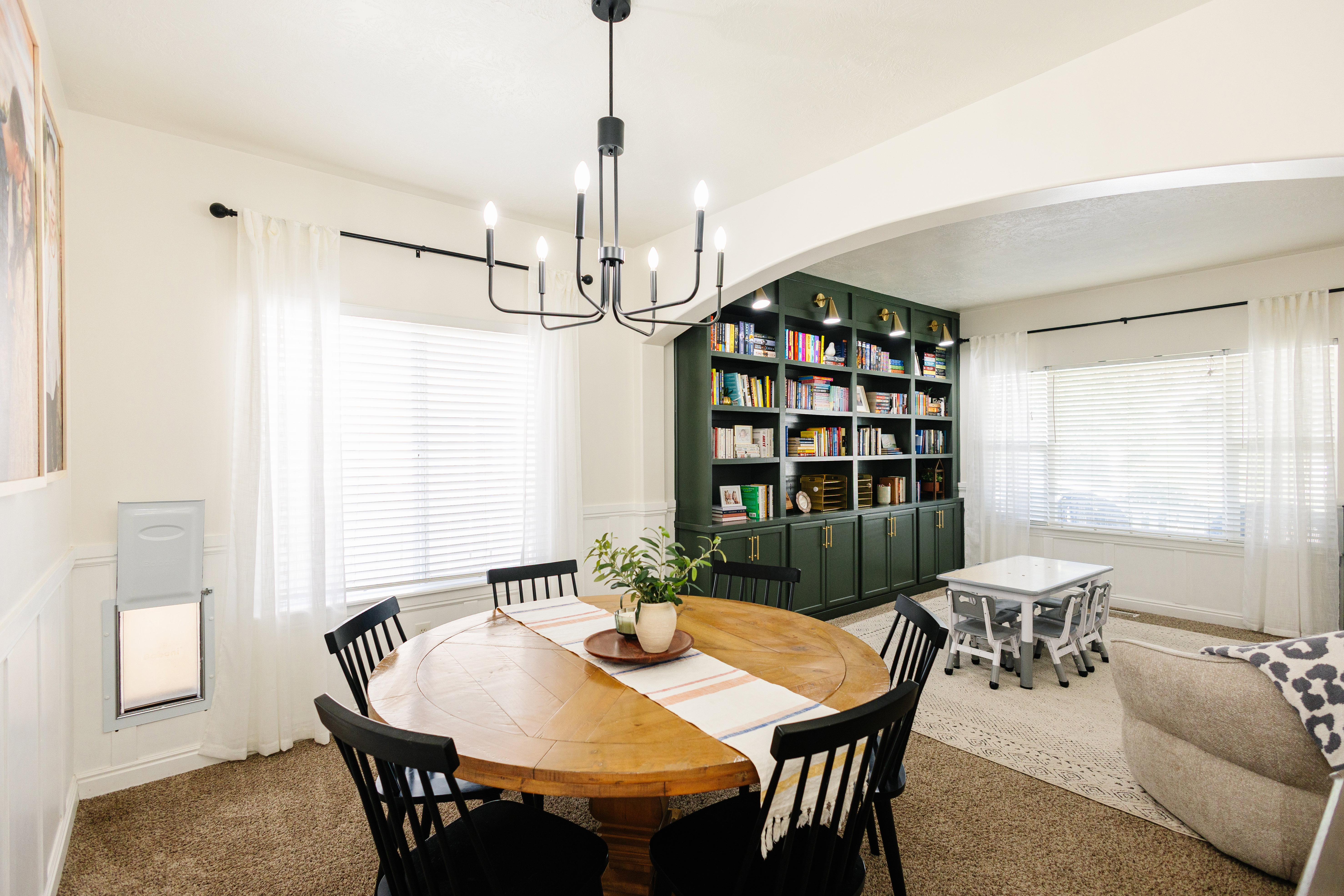 Dining area featuring a contemporary black chandelier, window with white blinds, and wainscoting