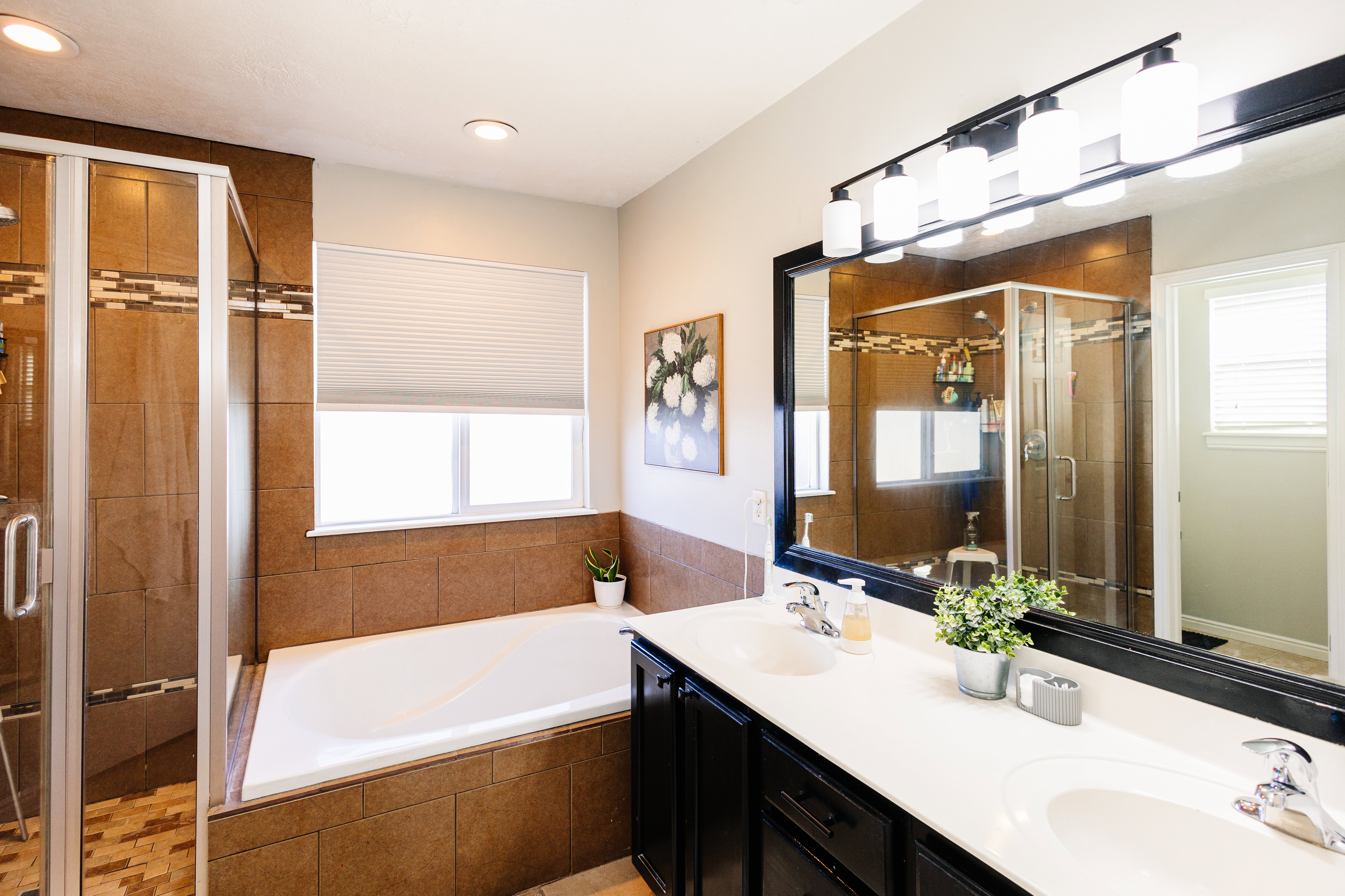 Bathroom featuring a built-in soaking tub, a stand-up shower with glass enclosure, and a dual-sink vanity with dark wood-finish cabinetry