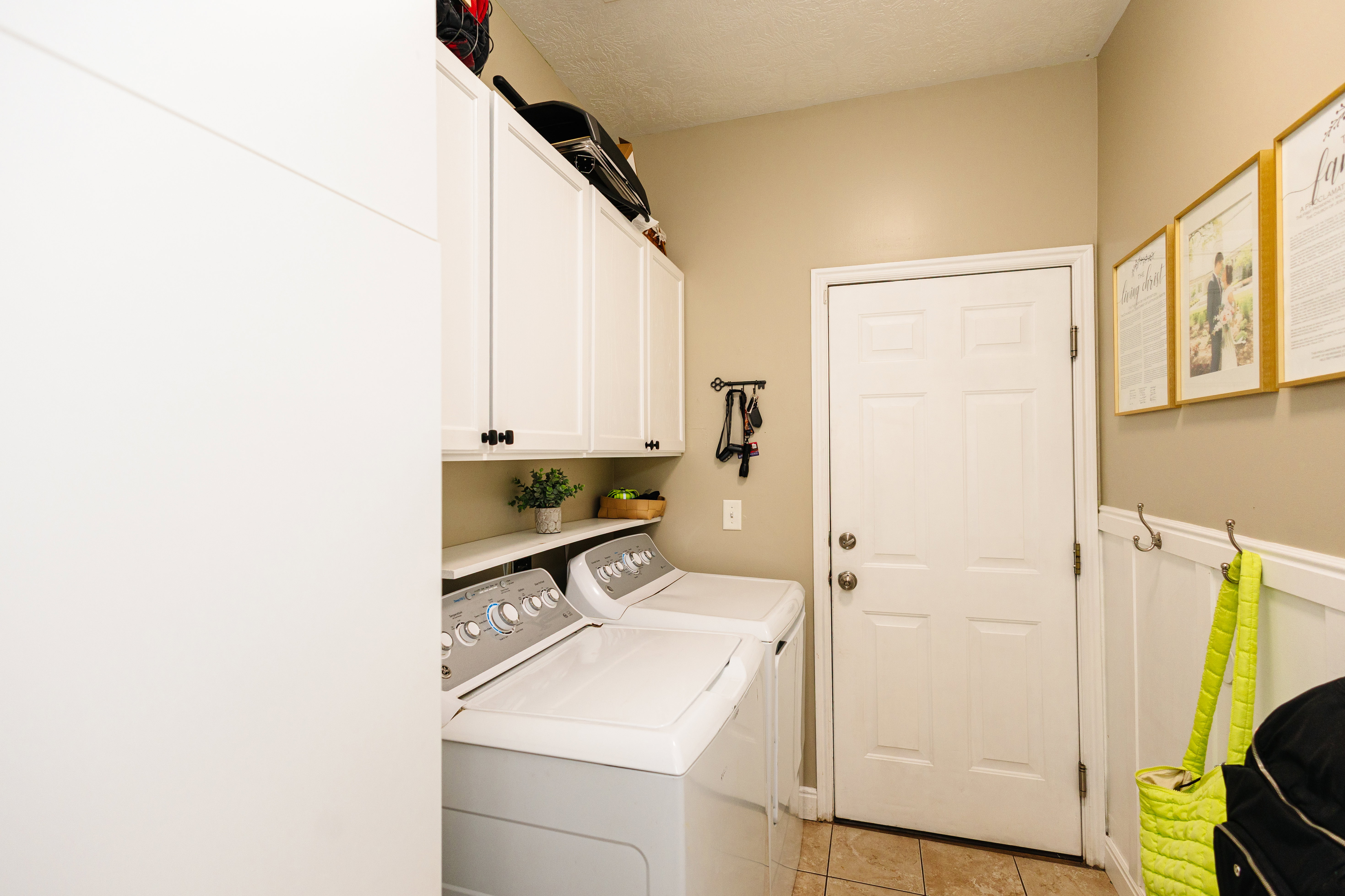 Laundry area featuring upper cabinetry with black hardware, open shelving, tile flooring, and a white paneled door