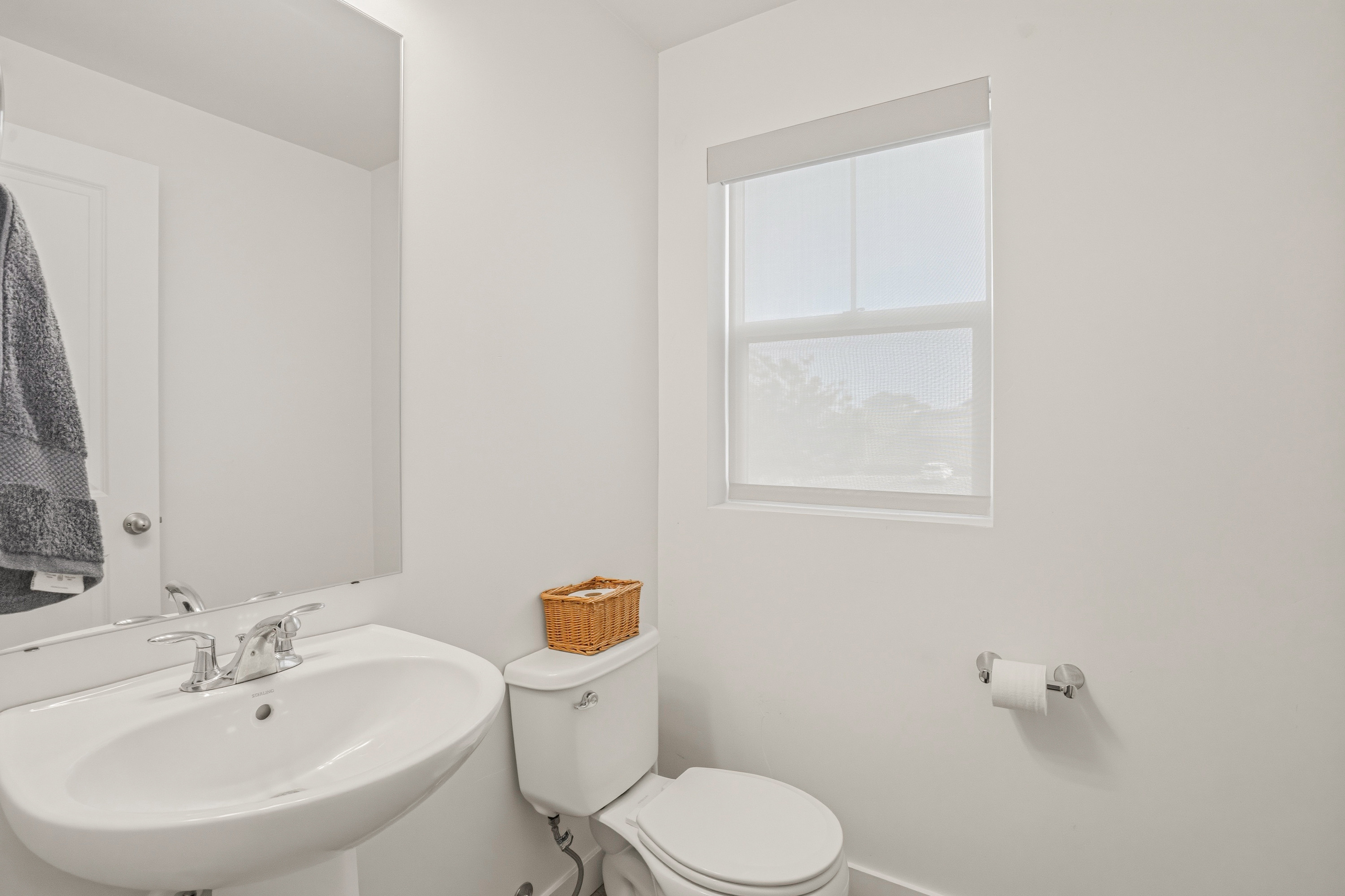 Pedestal sink with chrome faucet, large frameless mirror, and neutral wall paint